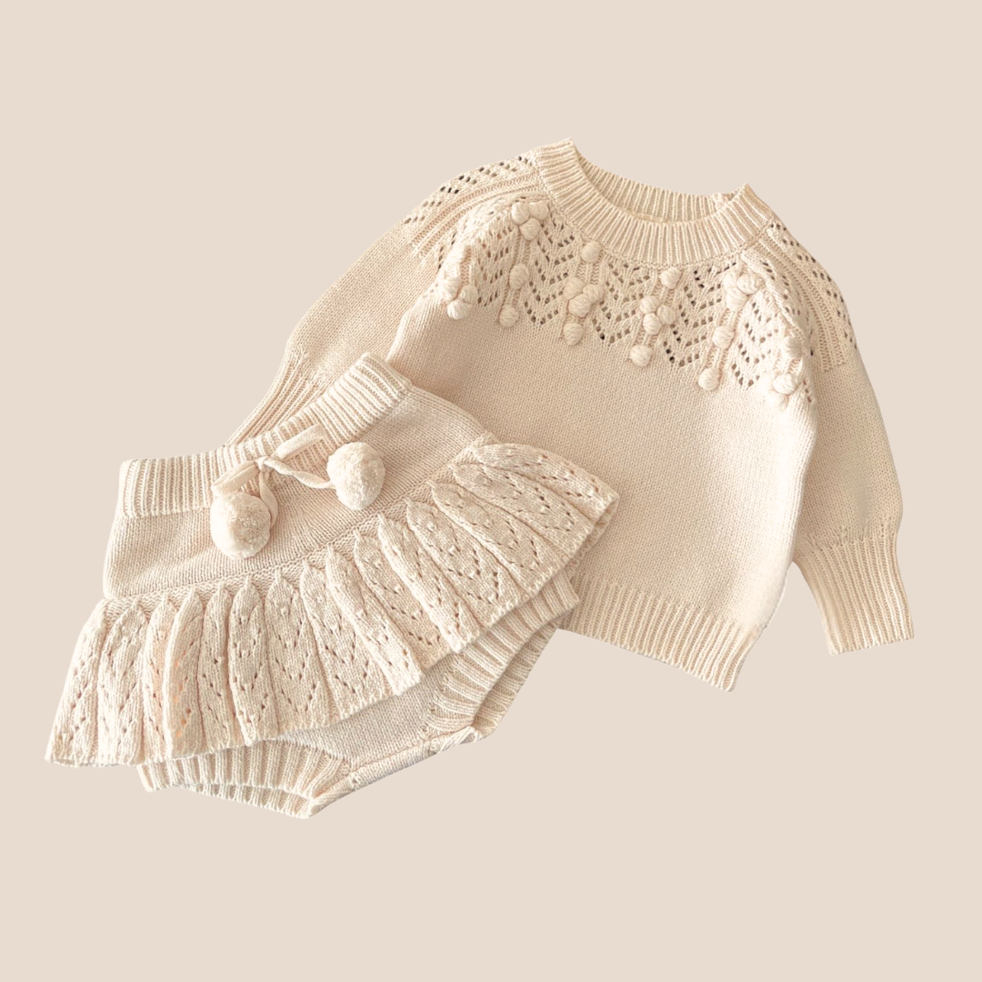 Cream-colored knitted outfit with matching hat on a light beige background