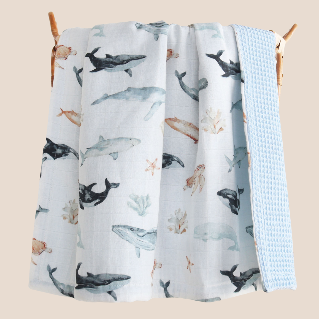 lose-up of ocean animals print with whales, turtles, dolphins, and coral – soft bamboo baby muslin- hanging on nursery rack