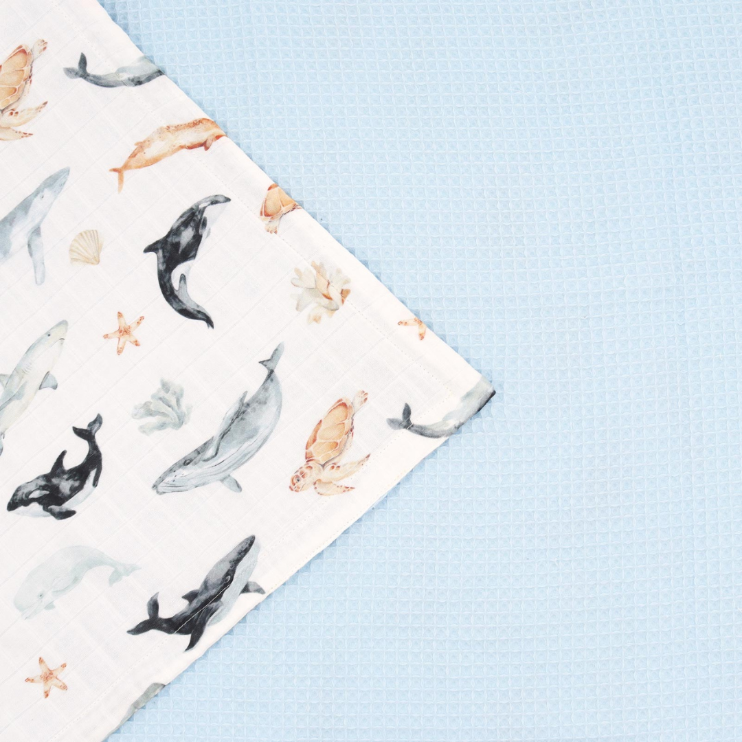 Flat lay of reversible ocean baby blanket with full view of muslin front and waffle back – baby gift idea