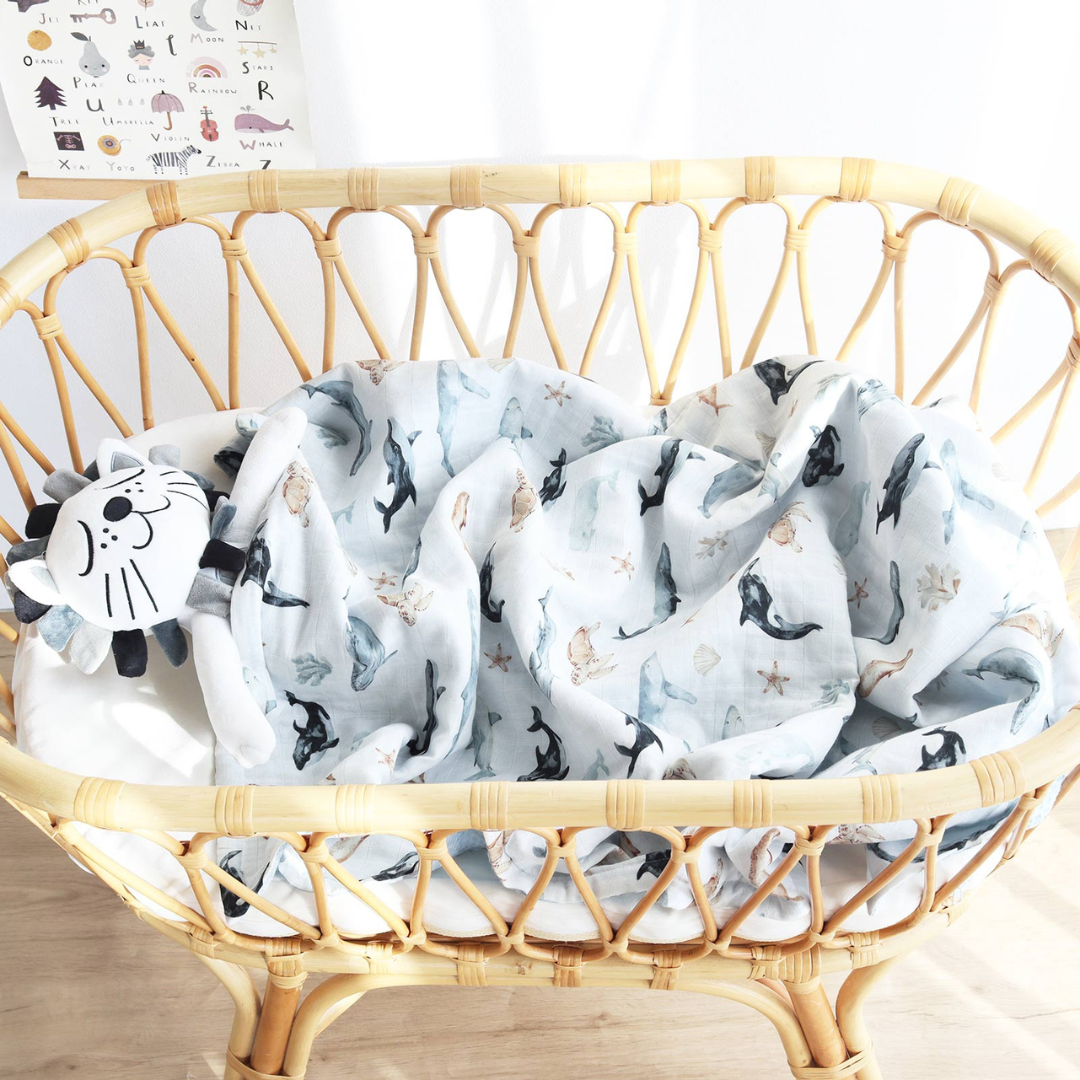 Baby swaddled in ocean sea creature blanket inside rattan bassinet – coastal baby nursery must-have