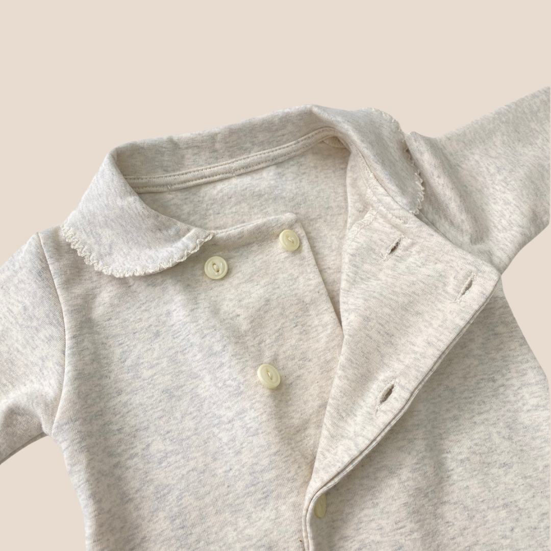 Close-up of a gray baby onesie with button details on a beige background