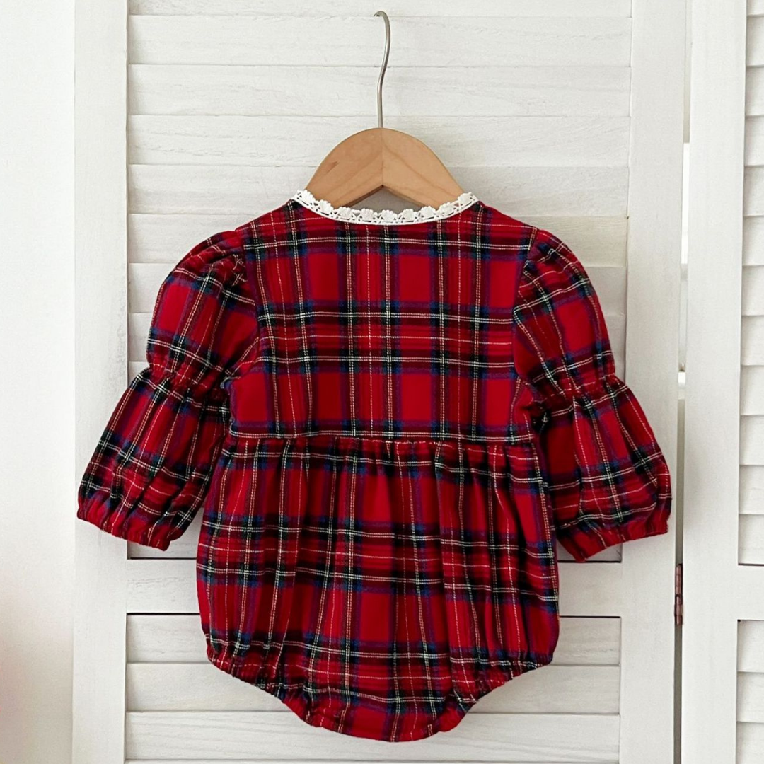 Red plaid baby romper on a wooden hanger against a white wooden panel background