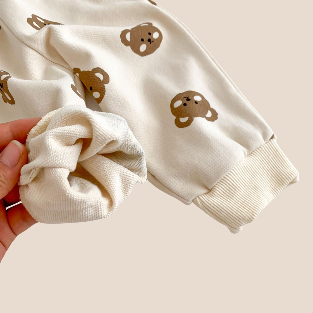 Baby outfit with bear patterns and a matching scrunchie on a beige background