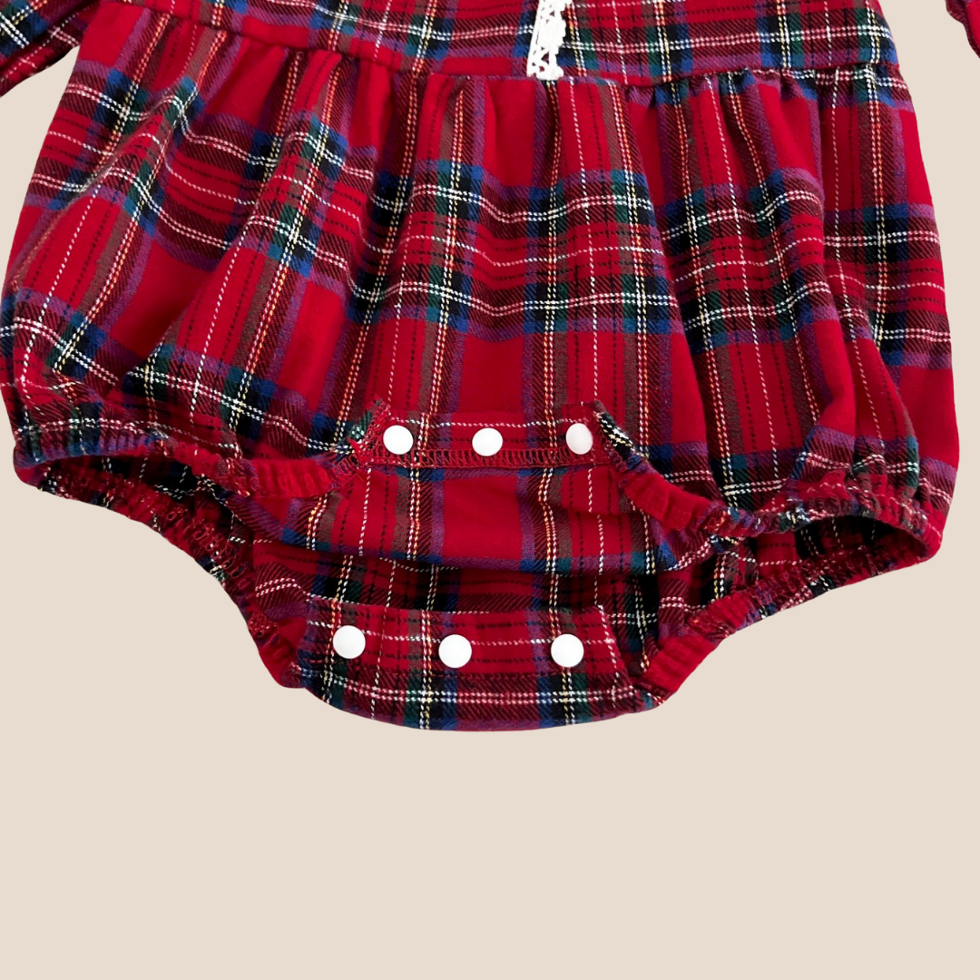 Red plaid baby bloomers with white buttons on a beige background