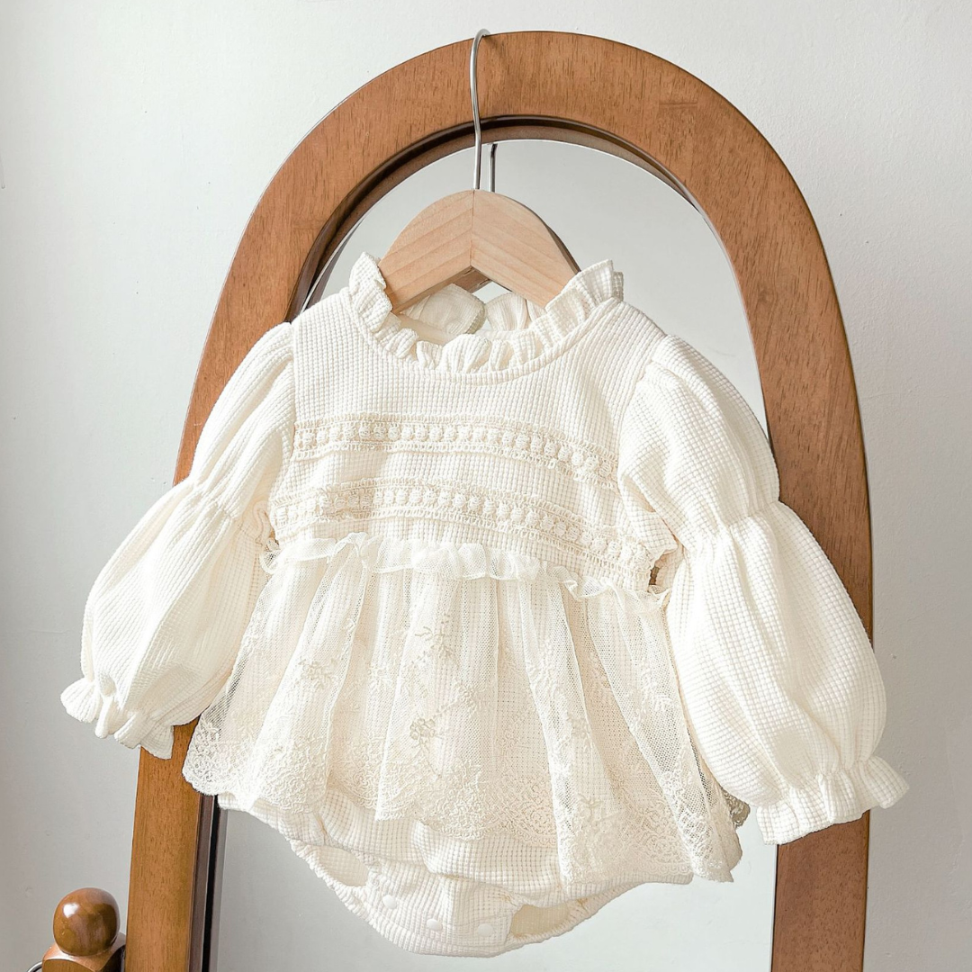 White baby romper with ruffled details on a wooden hanger against a white background
