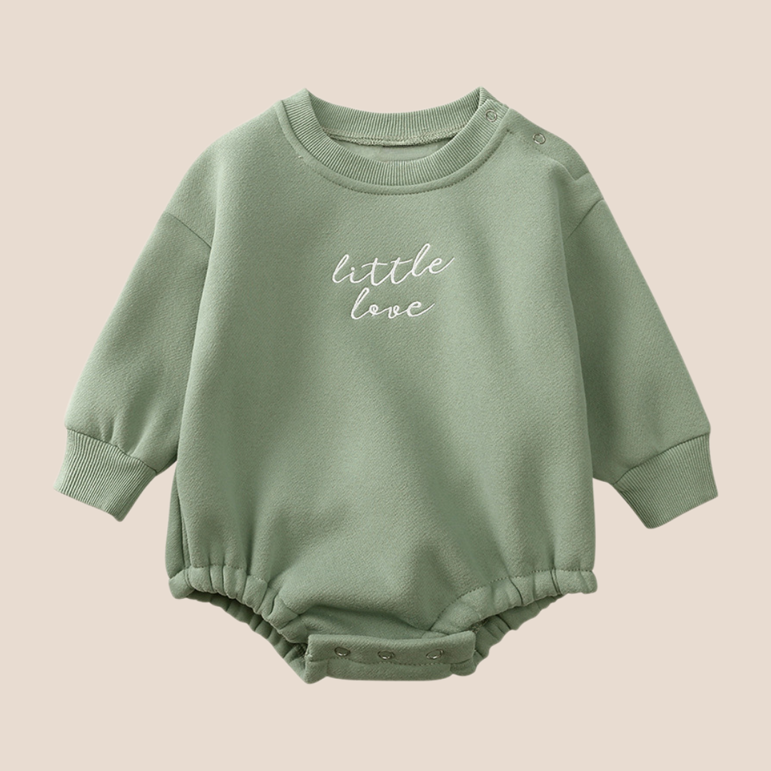 Green baby romper with 'little love' text on a beige background