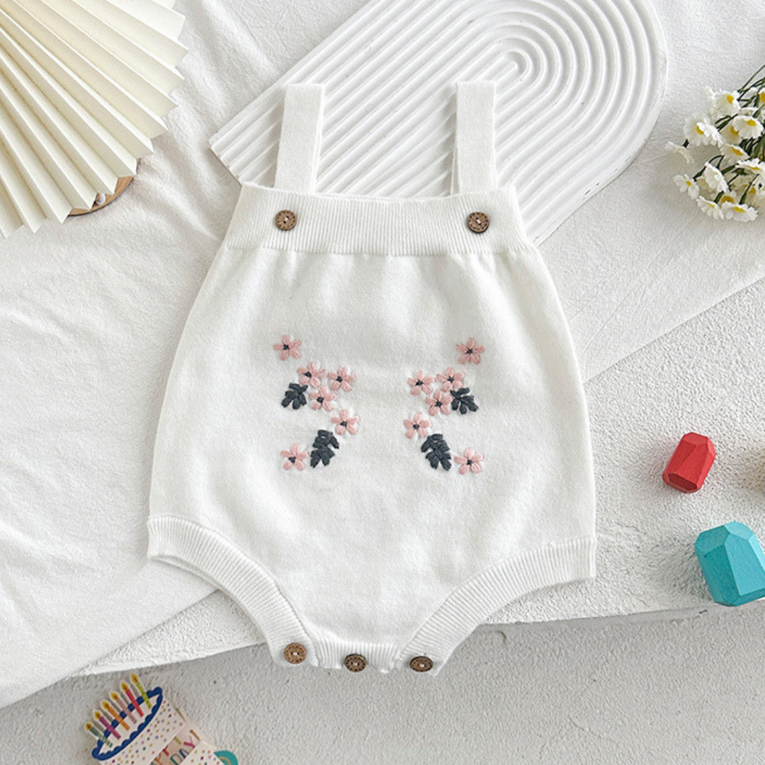 White baby romper with floral embroidery on a textured surface