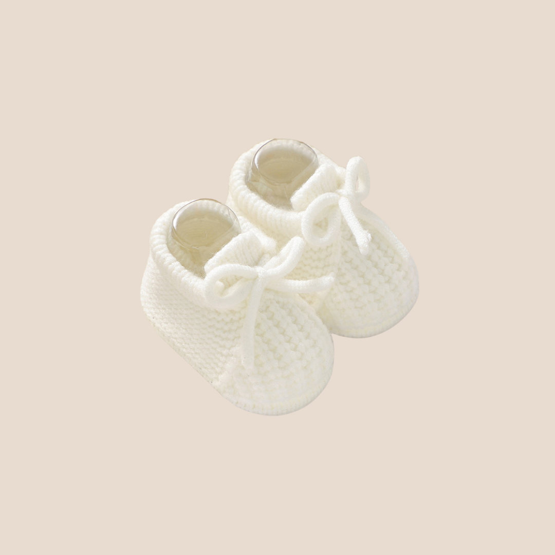 Pair of white baby booties on a beige background