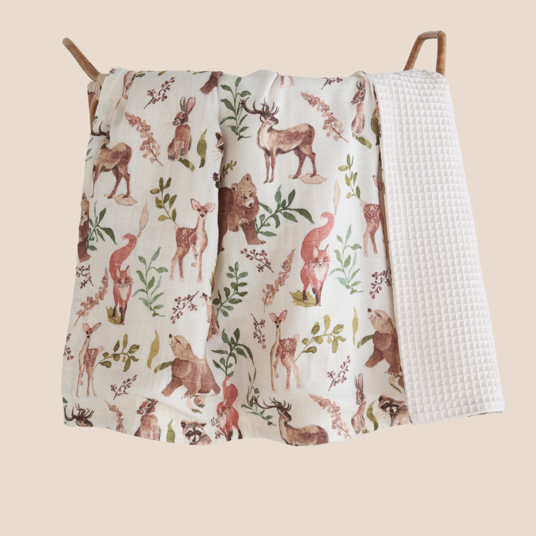 Folded reversible baby blanket with cotton waffle and woodland print – sustainable and soft baby bedding. Perfect baby shower gift idea for making personalized baby shower gift boxes for loved ones and clients.