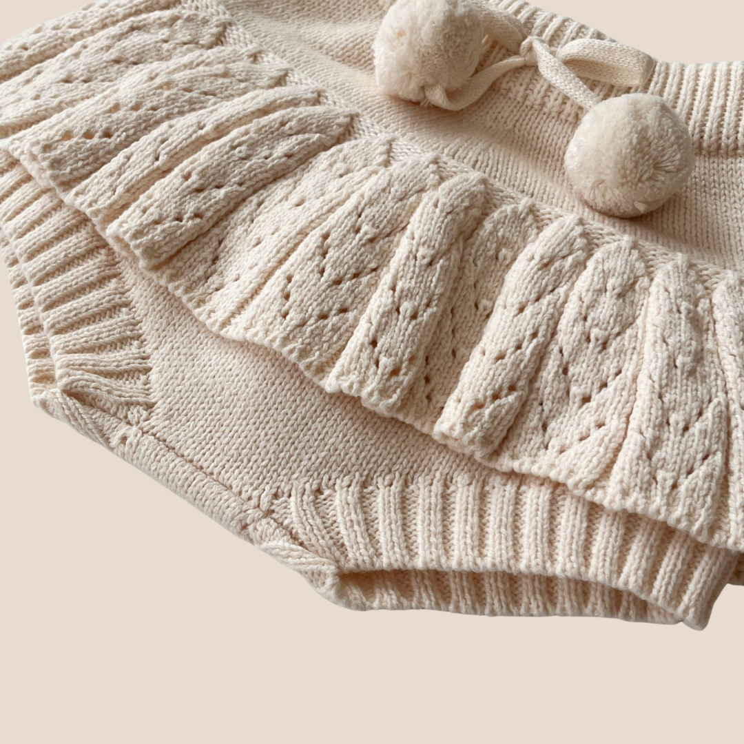 Beige knitted skirt with cable pattern and pom-poms on a beige background