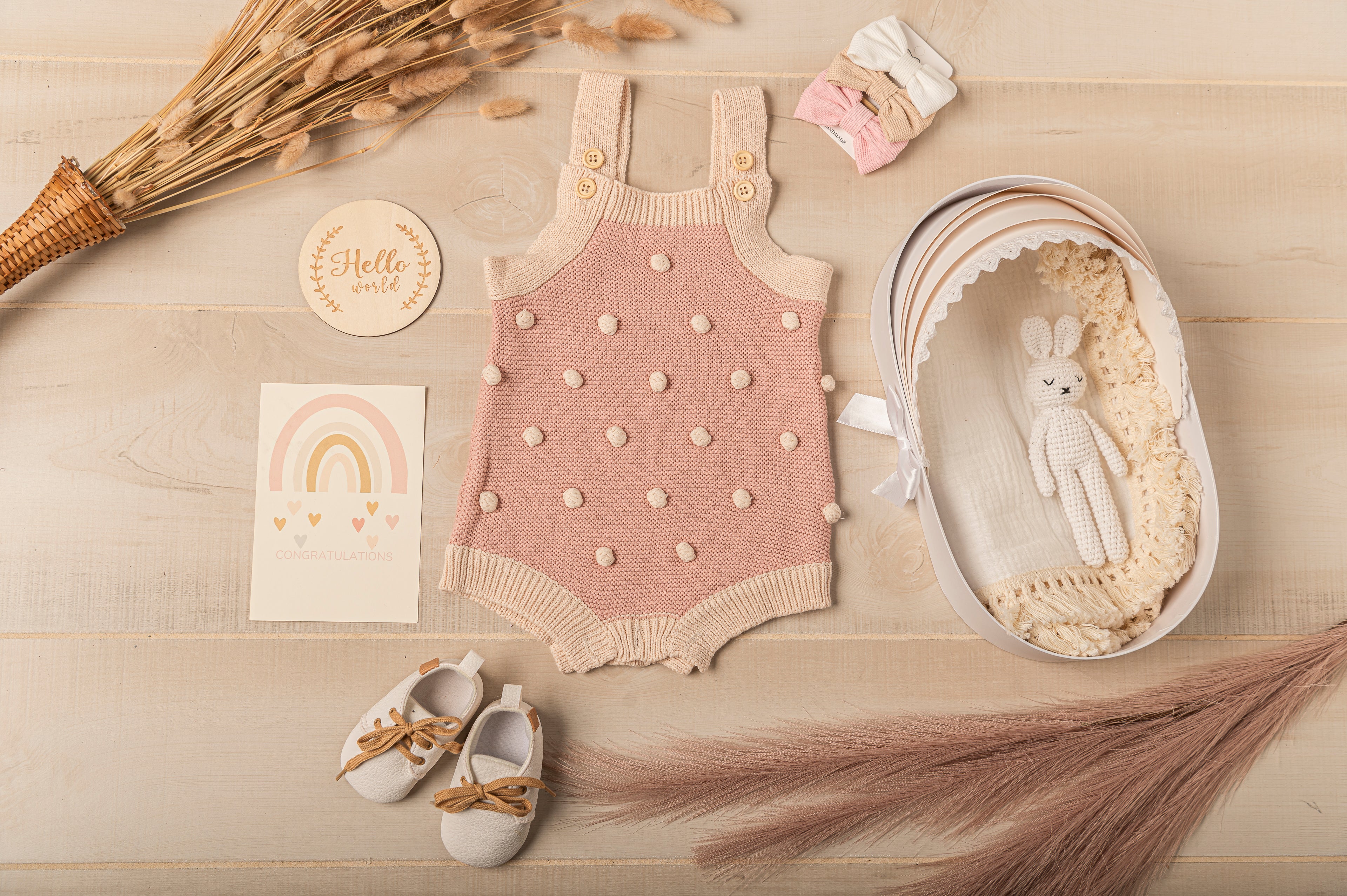 Neutral baby girl gift set with pink knitted romper, matching headbands, soft sole baby shoes, handmade crochet bunny toy, and muslin blanket in a luxury bassinet-shaped gift box. Perfect for baby shower gifts or newborn welcome gifts. Eco-friendly and customizable.