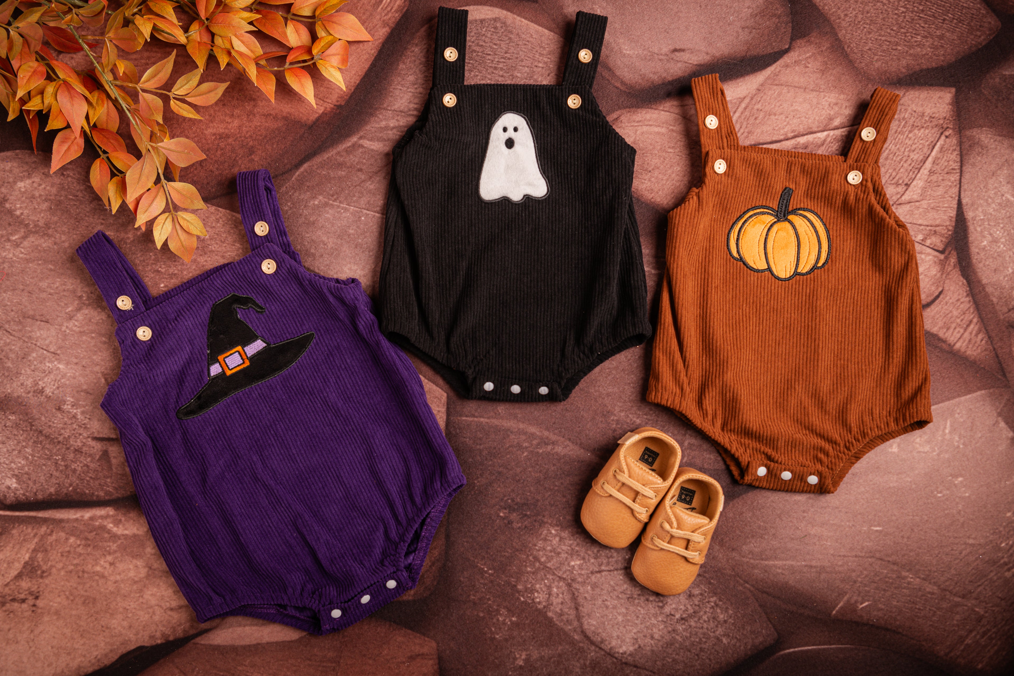 Three baby rompers with Halloween-themed designs on a textured surface.