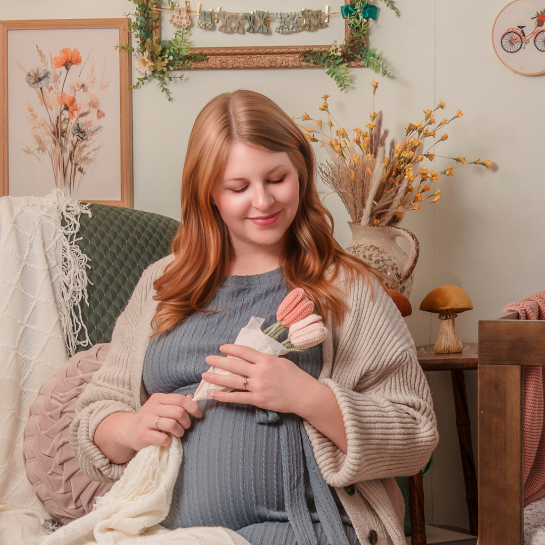 Woman holding a baby outfit in a cozy room with decorative elements.