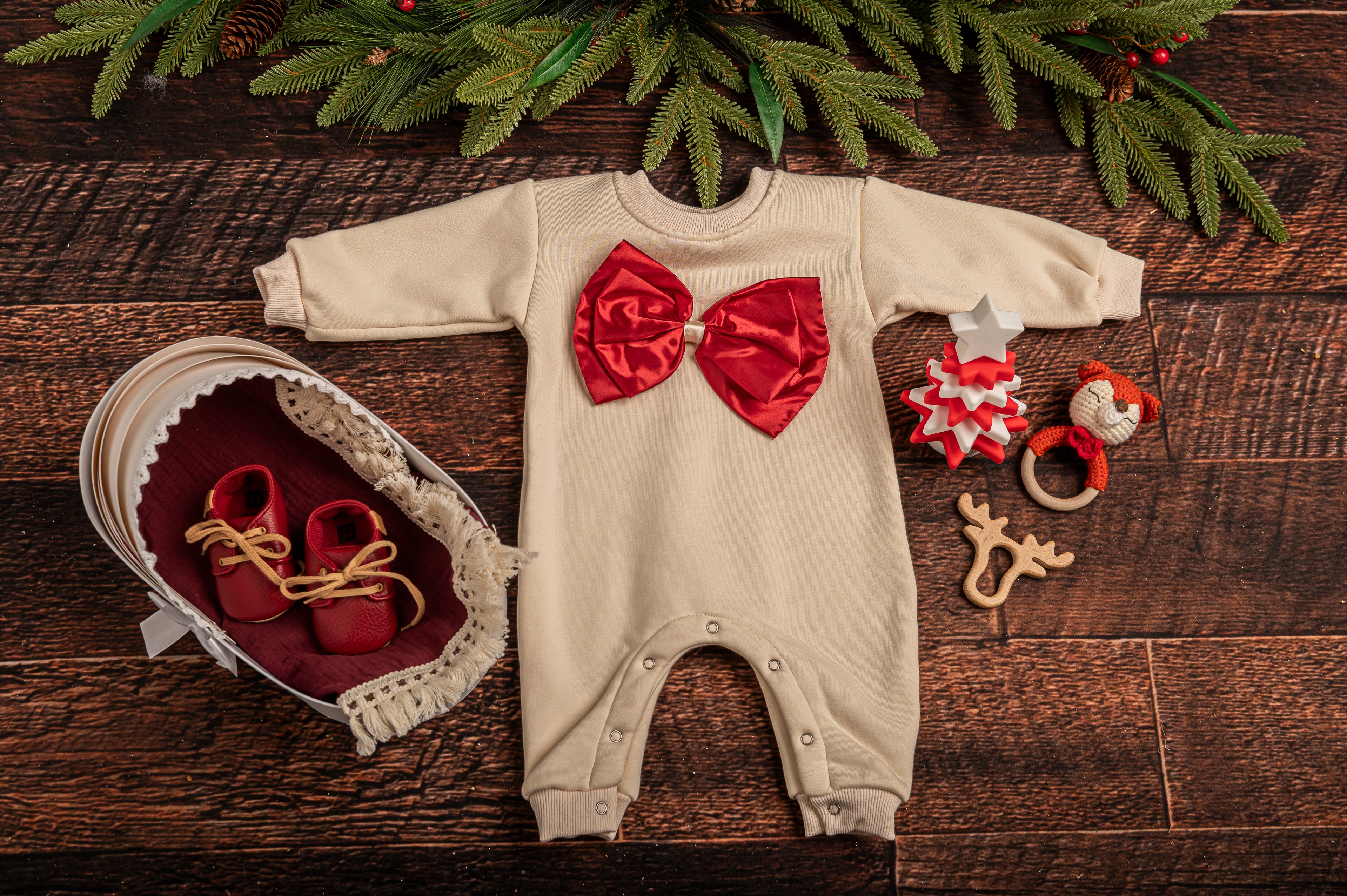 Cotton Craft Luxe Baby Girl Holiday Gift Basket with festive romper, cotton swaddle, leather shoes, hand-knitted rattle, wooden teether, and silicone Christmas tree toy. white romper