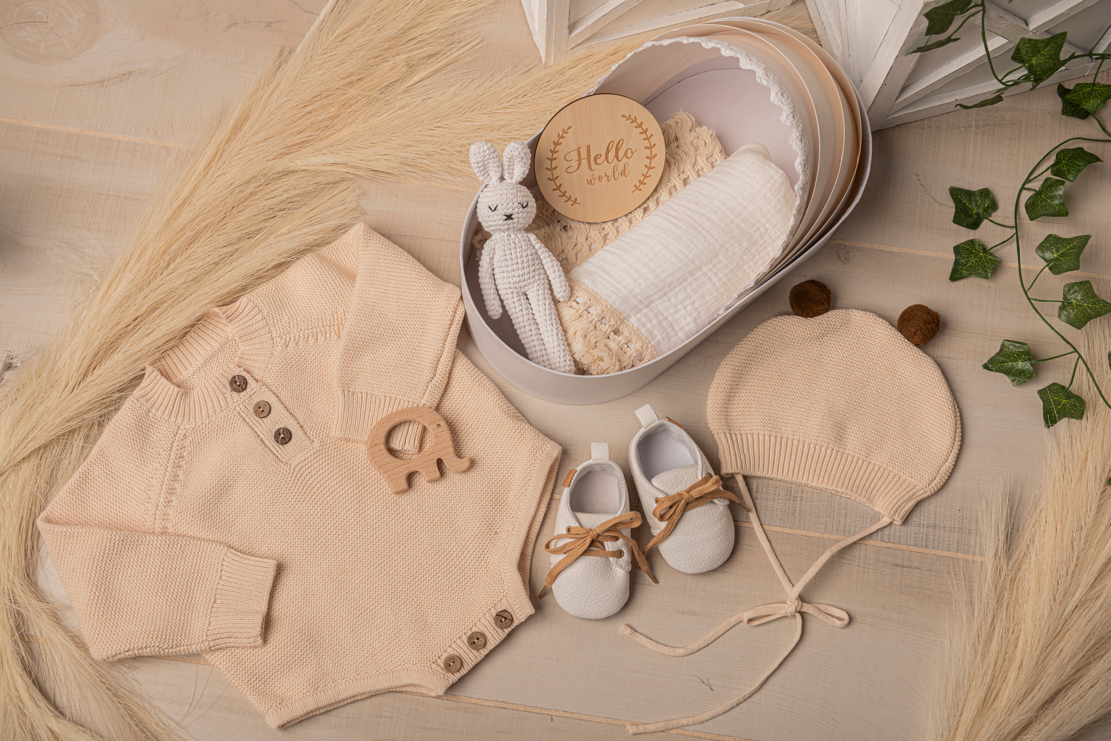 Ultimate newborn baby gift set with beige knit romper, wooden elephant rattle, soft leather shoes, bear ear hat, muslin wrap, and baby-safe crochet plush in a luxury bassinet box. Personalized baby gift idea for baby showers or hospital visits.