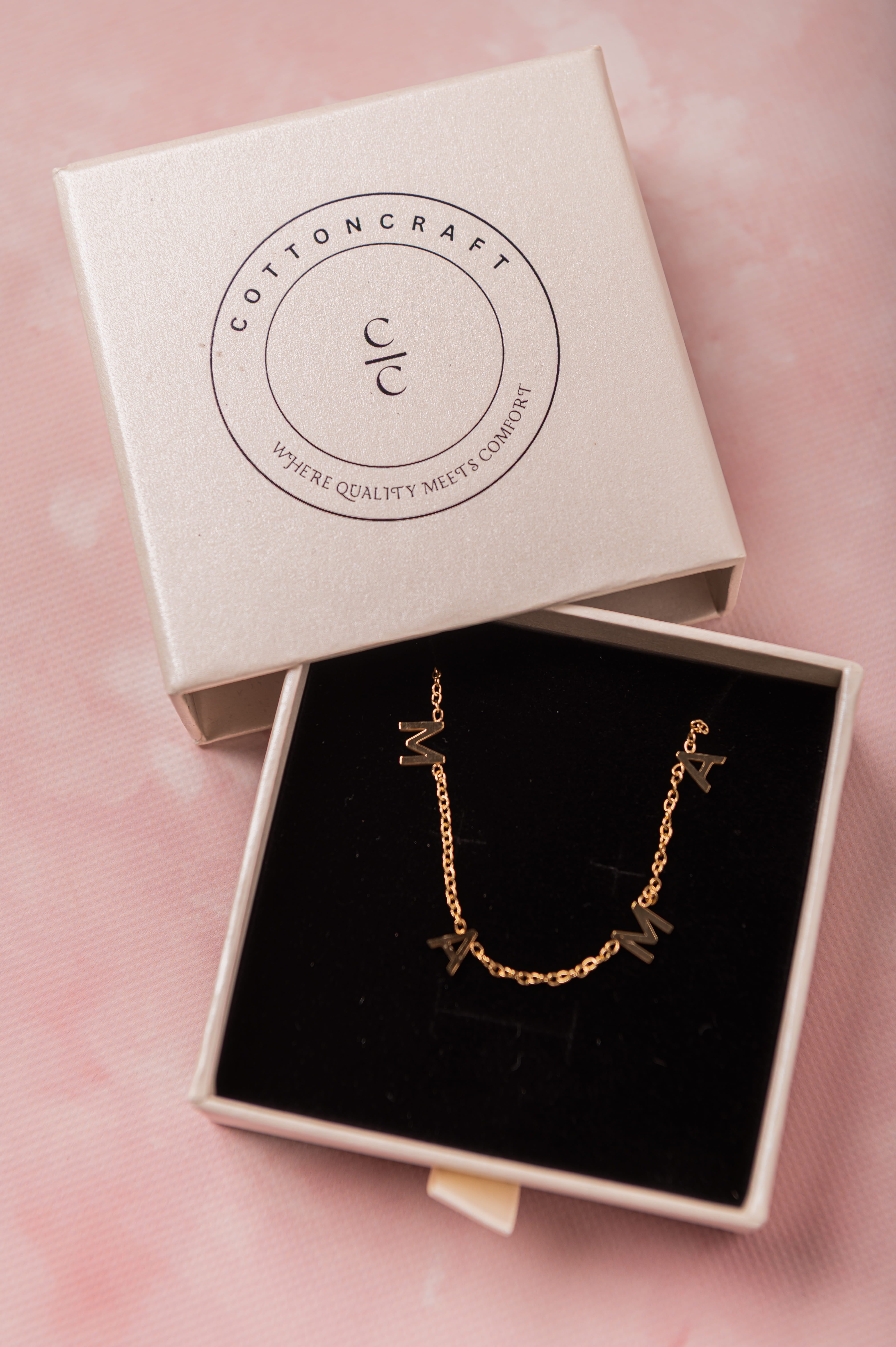 Gold necklace in an open Cotton Craft box on a pink background
