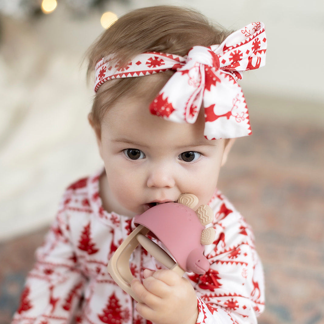 Baby wearing a red and white patterned outfit with a matching headband, holding a pink teething toy.