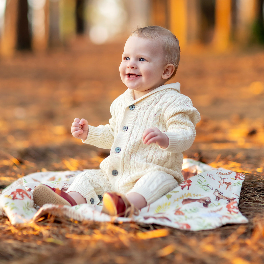Baby sitting on a blanket in a forest with autumn leaves