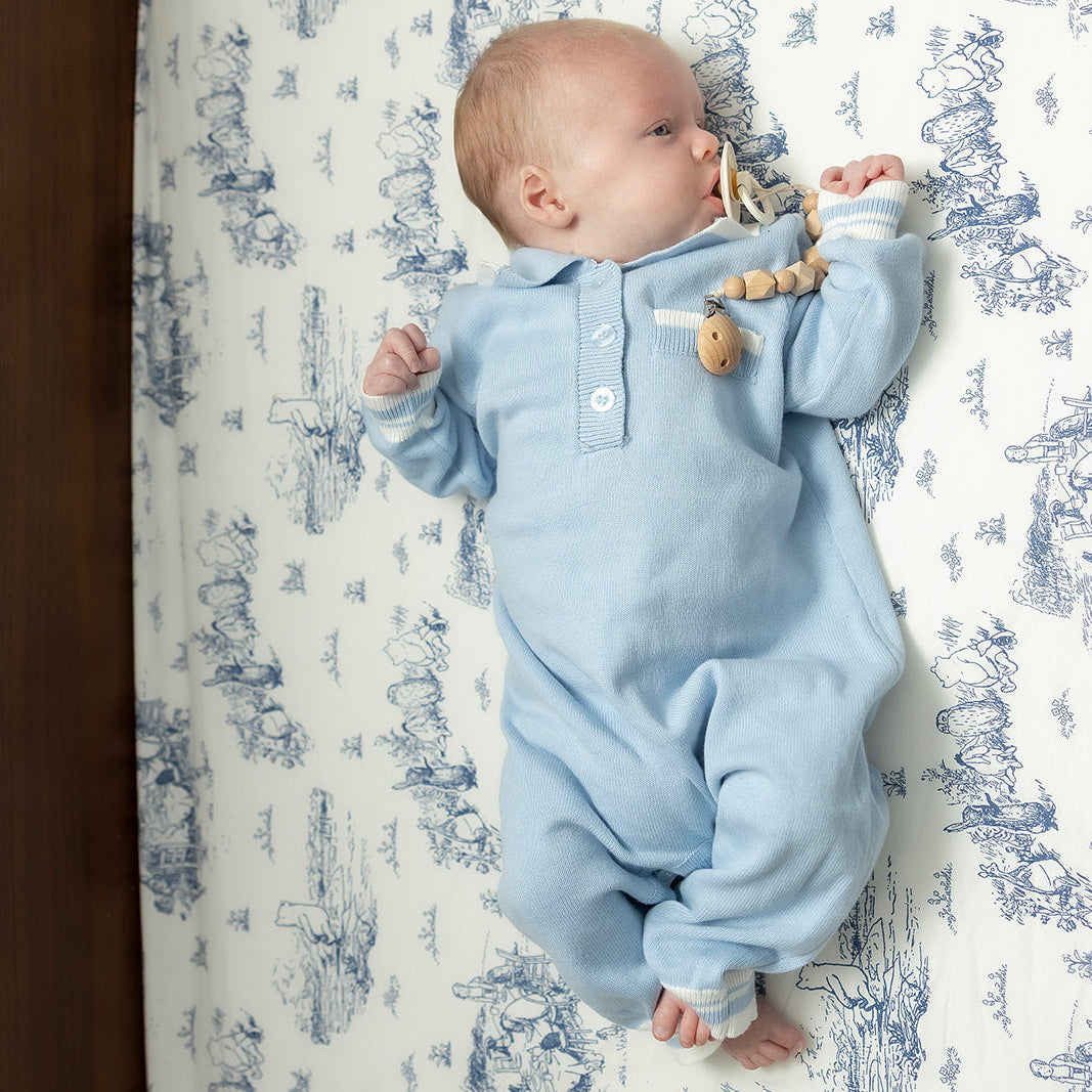 Baby in a blue outfit lying on a patterned mattress