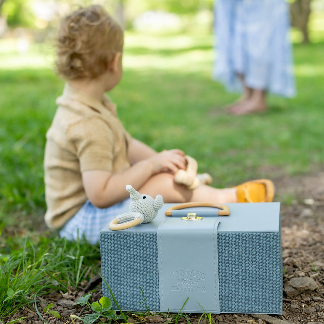 Child sitting on a box with toys, looking at a pregnant woman in a park.