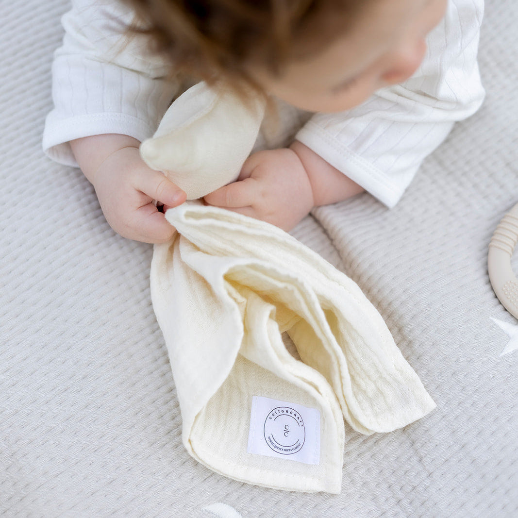 Baby holding a white cloth with a label on a textured surface