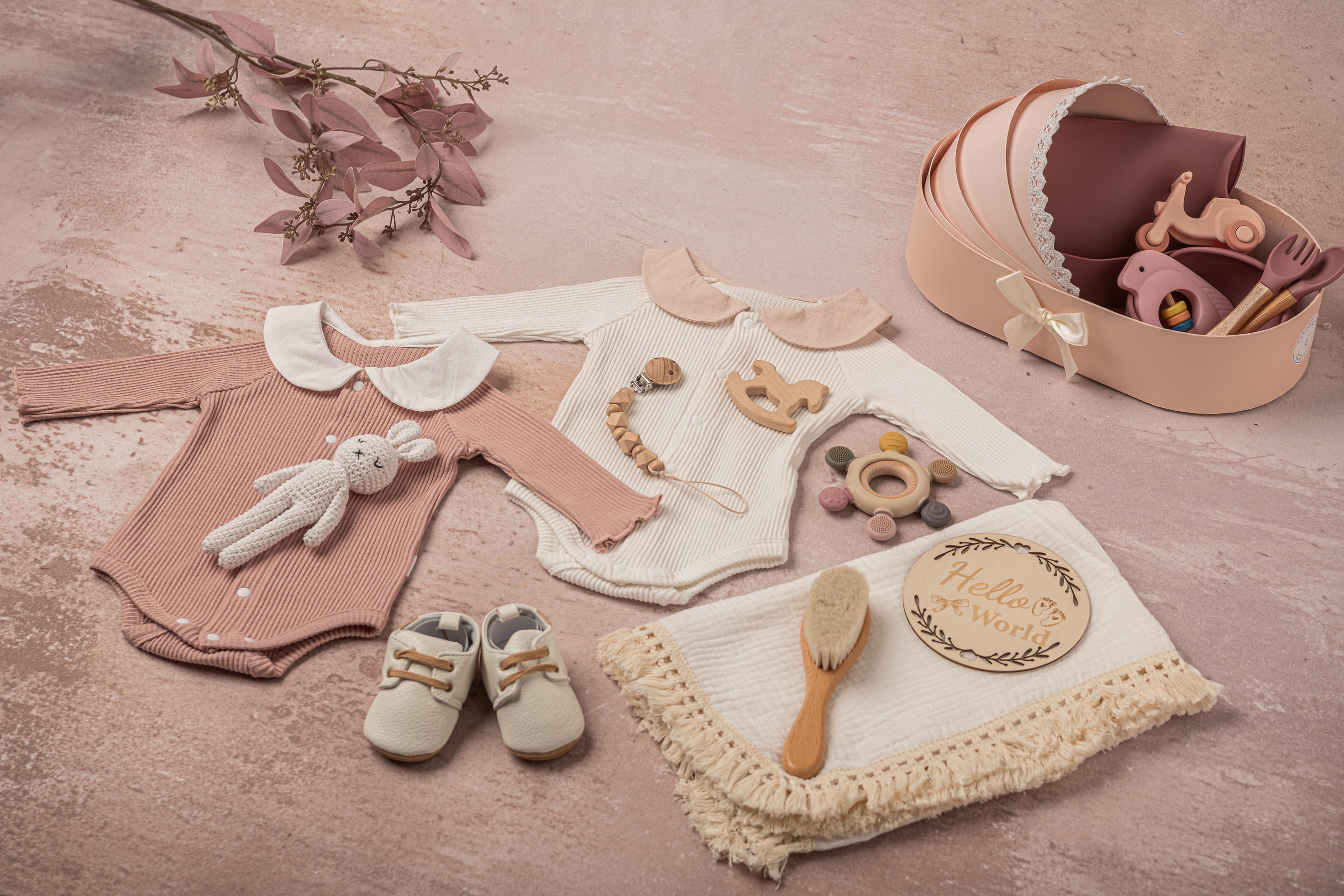 Luxury baby girl gift basket presented in a crib-shaped keepsake box, wrapped in delicate ribbon, containing premium cotton outfits, a hand-knitted bunny, wooden and silicone teething toys, and mealtime essentials.