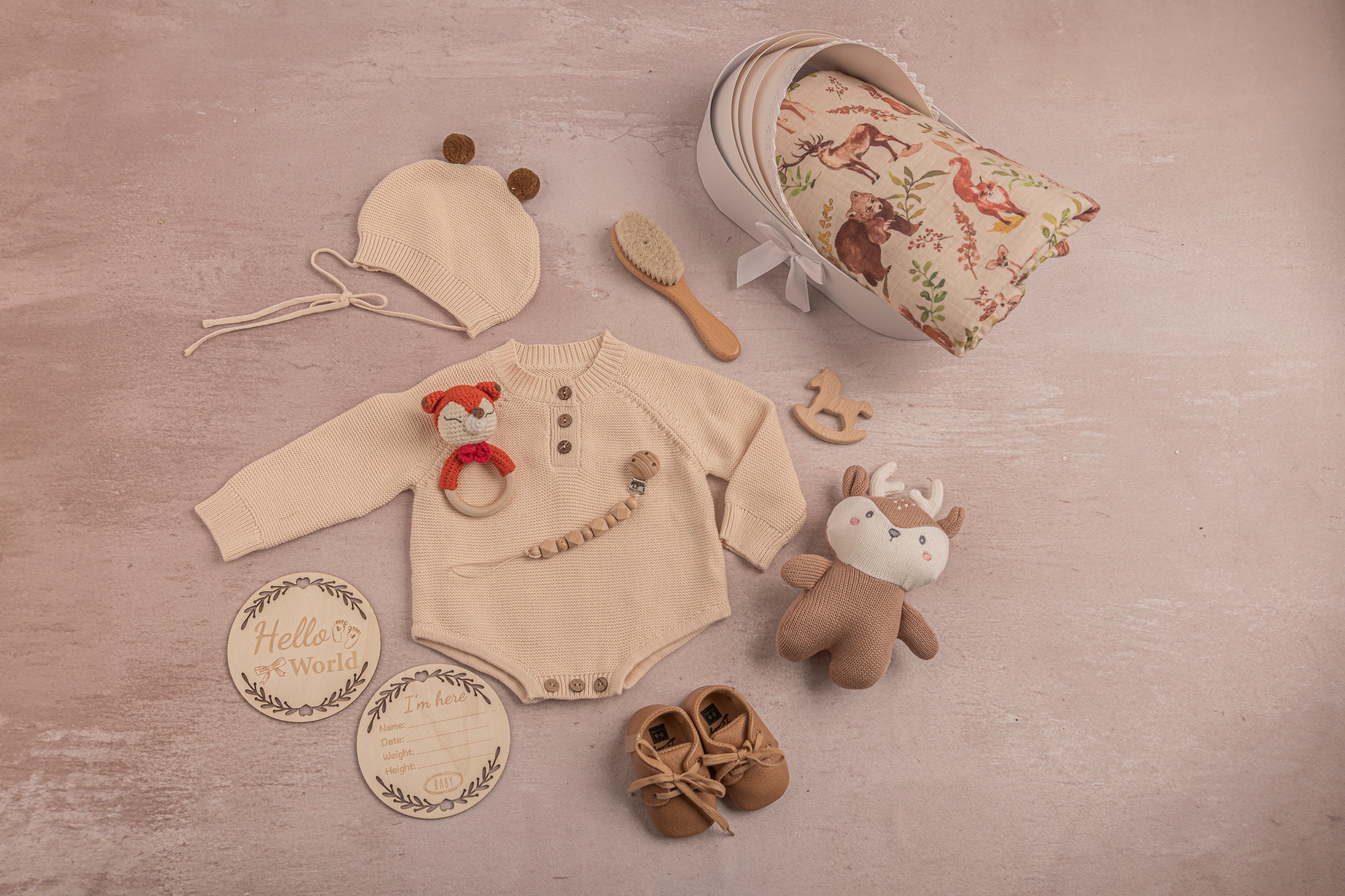 Collection of baby items including a onesie, hat, shoes, and toys on a wooden surface.