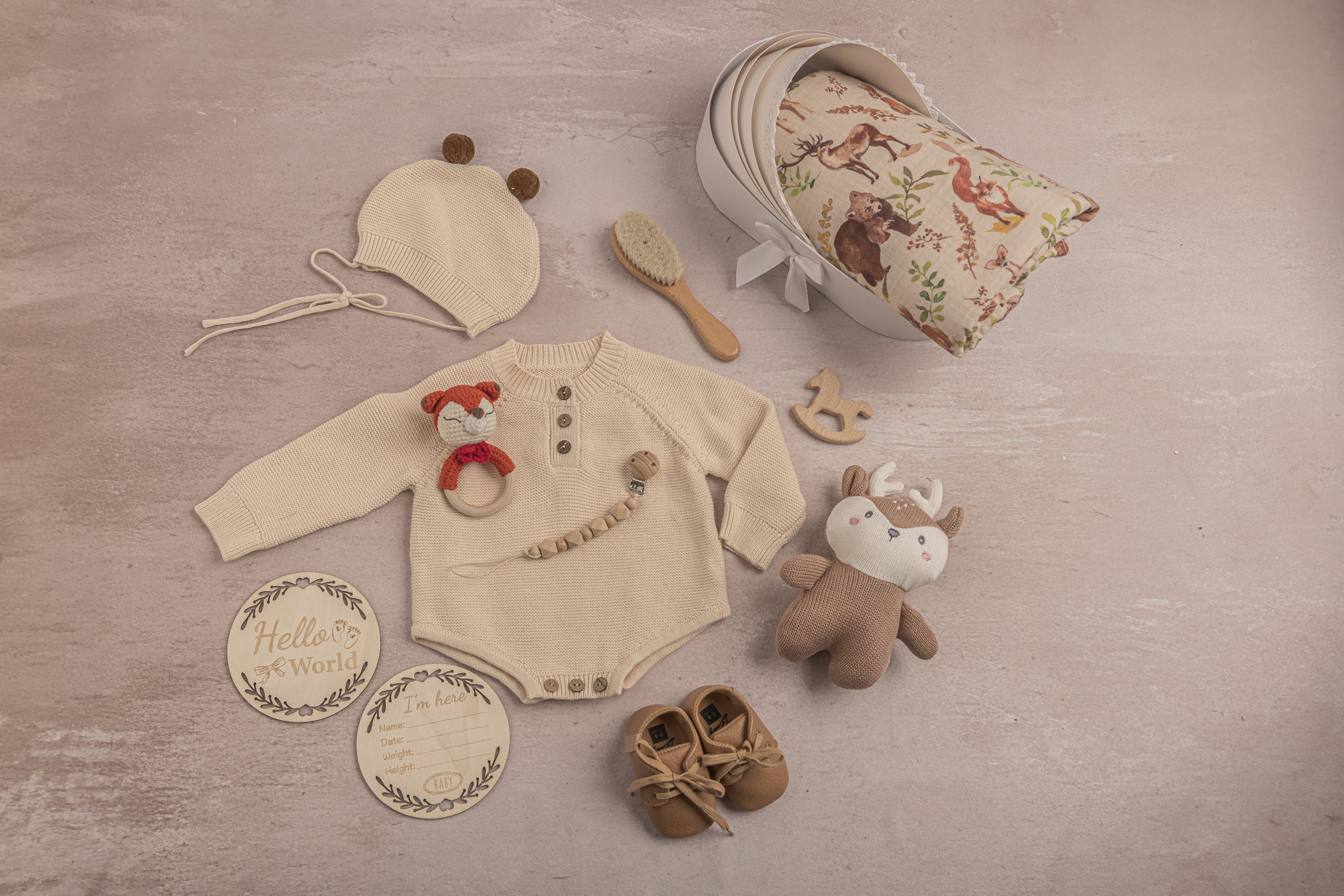 Collection of baby items including a onesie, hat, shoes, and toys on a wooden surface.