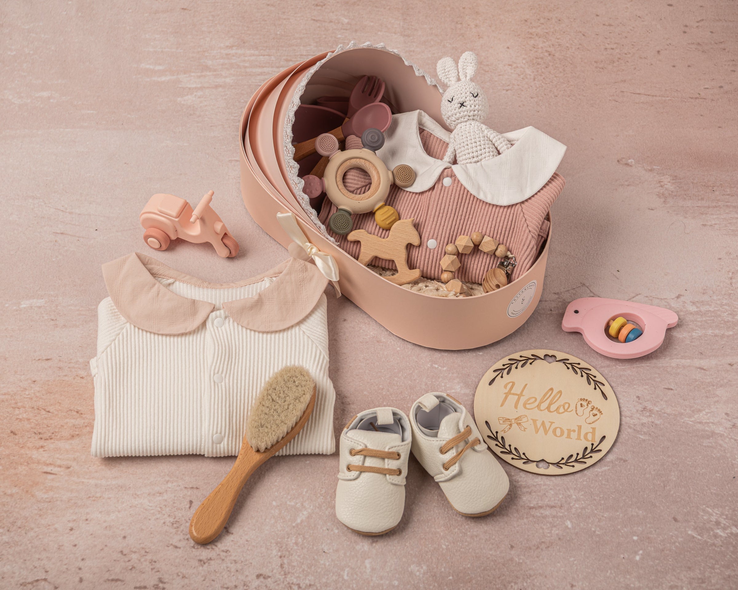 Exquisite baby girl gift set in soft pink and white, featuring 100% cotton outfits, a fringed swaddle, leather baby shoes, handmade bunny plush, and sustainable wooden and silicone toys, elegantly arranged for a luxury gifting experience.