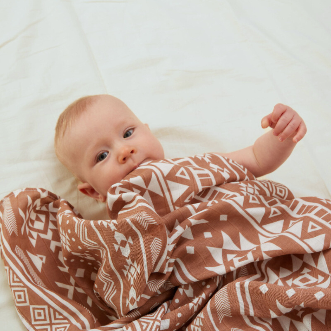Adorable baby wrapped in soft bamboo cotton swaddle blanket with tribal terracotta print – eco-friendly newborn essential ideal for customized baby shower gifts, luxury baby hampers, and personalized gifts for new moms. Breathable, gentle on skin, and perfect for everyday snuggles.