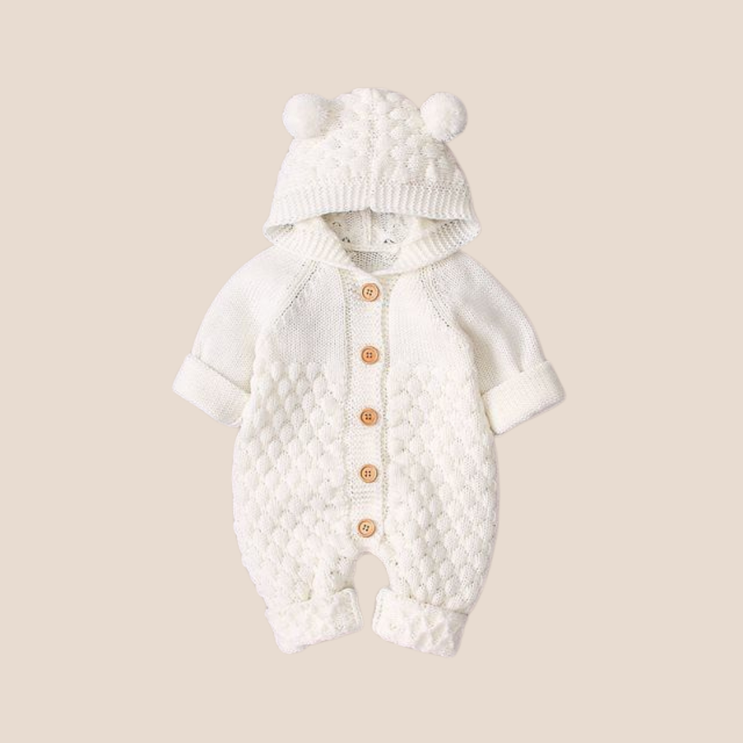 White baby romper with hood and pom-pom details on a beige background