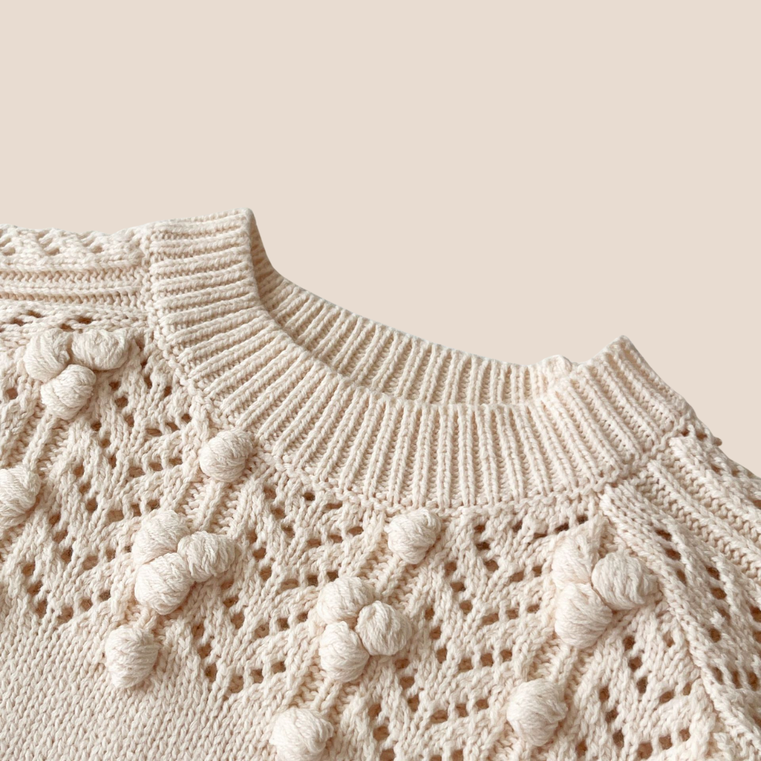 Close-up of a beige knitted sweater with decorative elements on a beige background