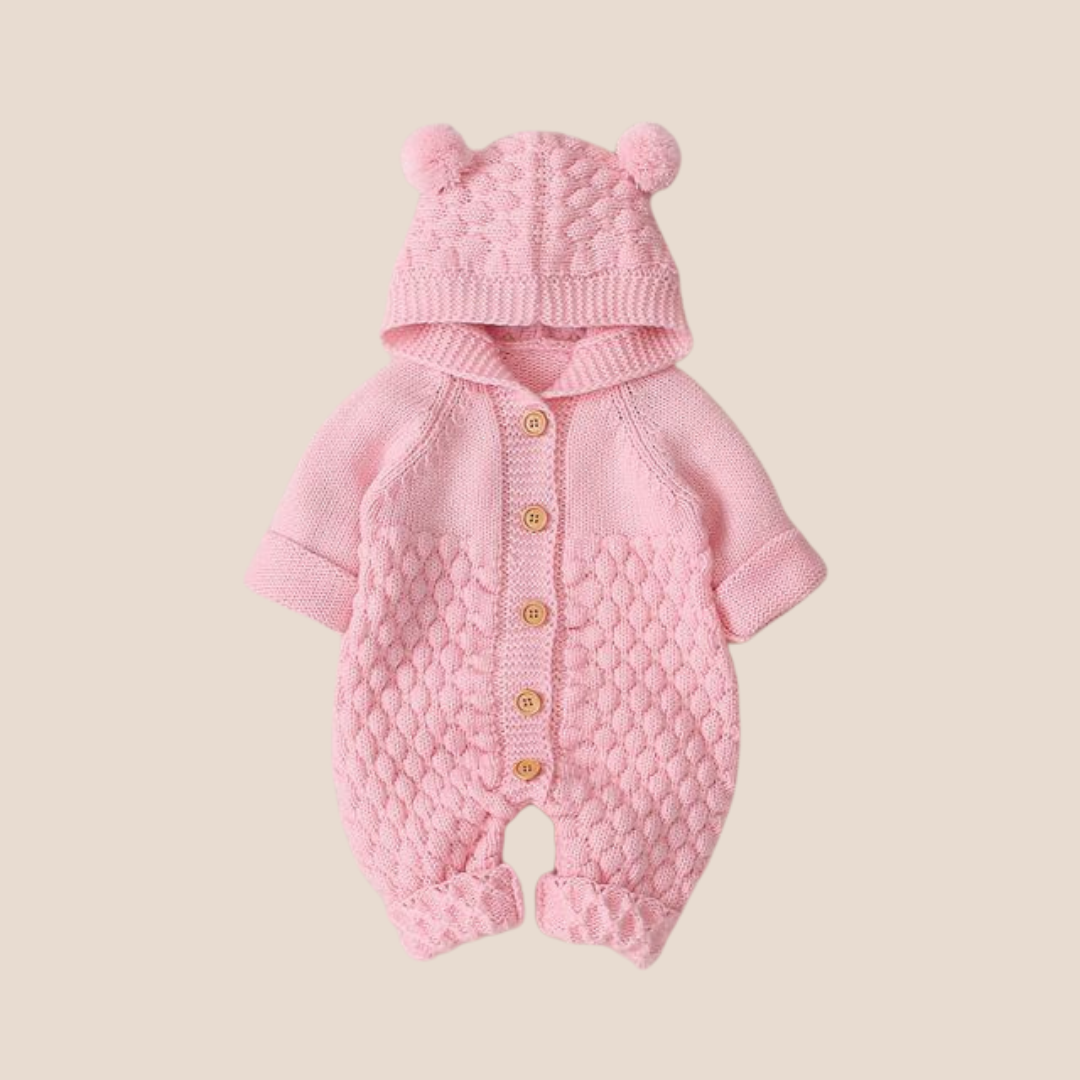 Pink knitted baby romper with matching hat on a beige background