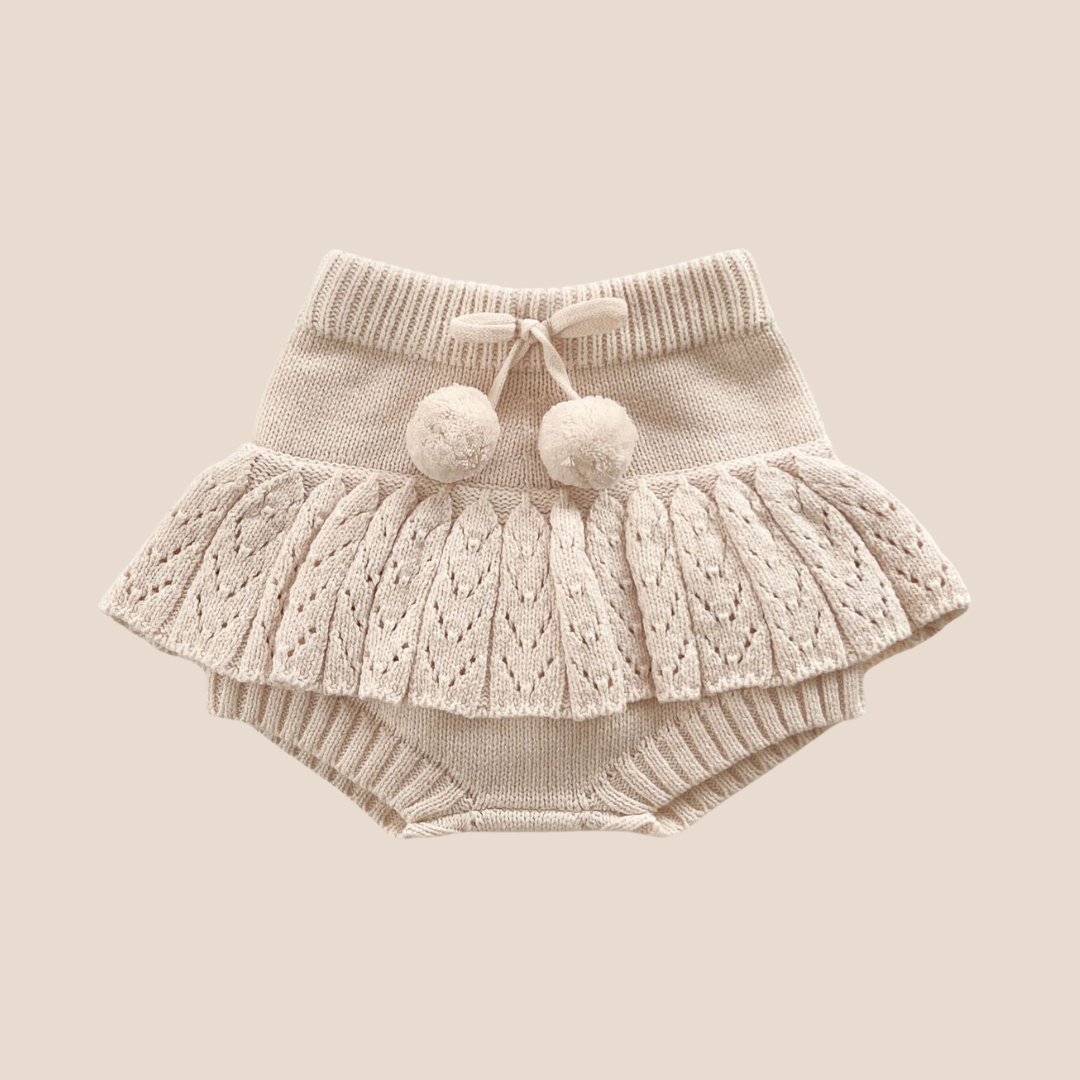 Knitted baby outfit with a skirt and bloomers on a beige background