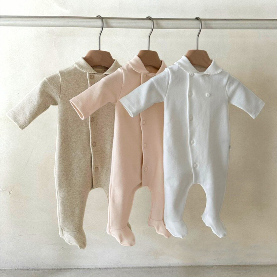 Three baby rompers hanging on a rack against a plain background
