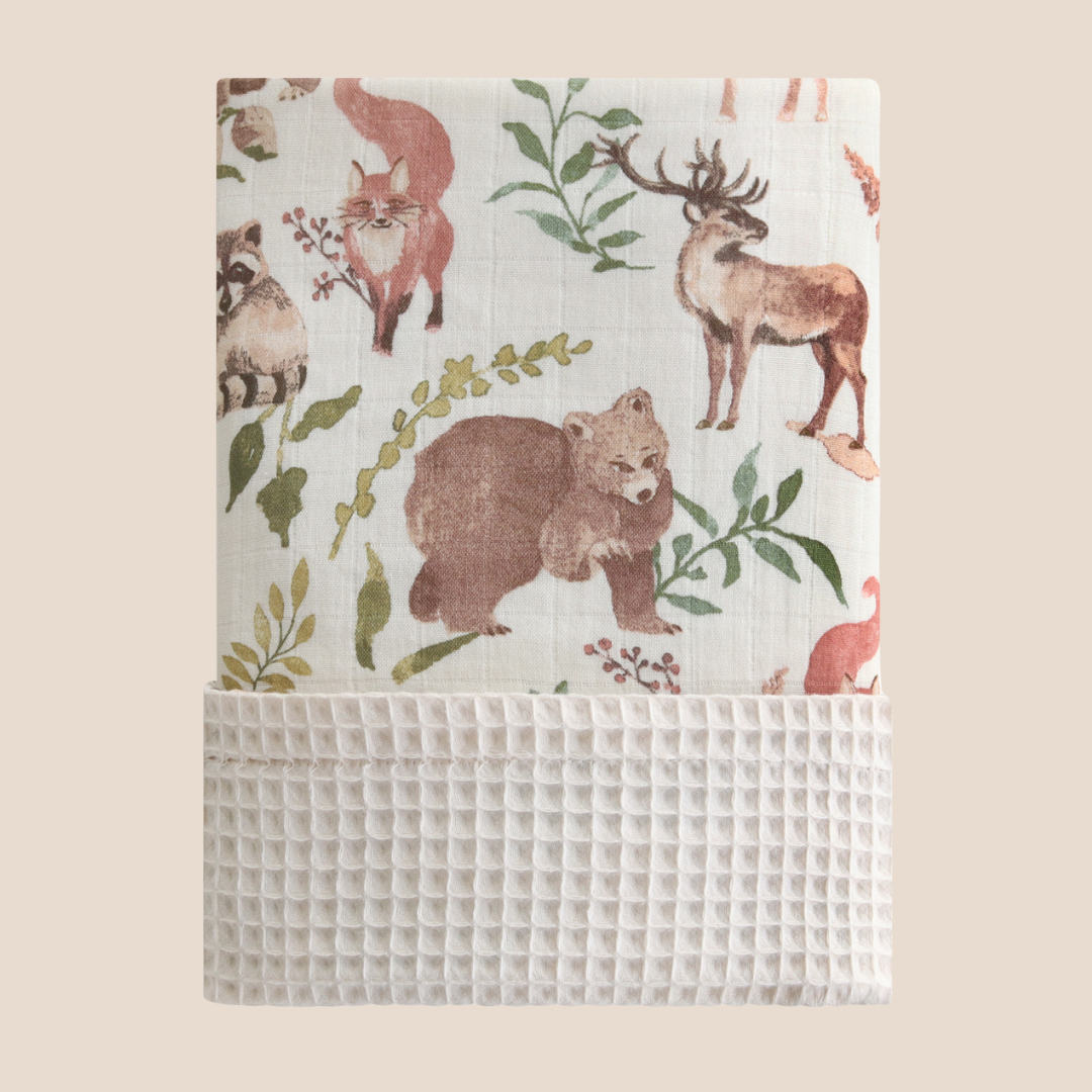 Folded reversible baby blanket with cotton waffle and woodland print – sustainable and soft baby bedding. Perfect baby shower gift idea for making personalized baby shower gift boxes for loved ones and clients.
