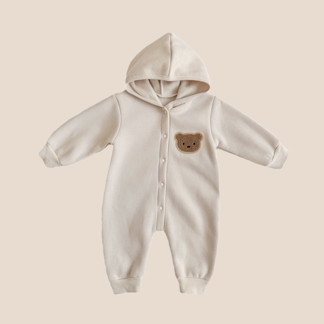 White baby onesie with a bear patch on a beige background