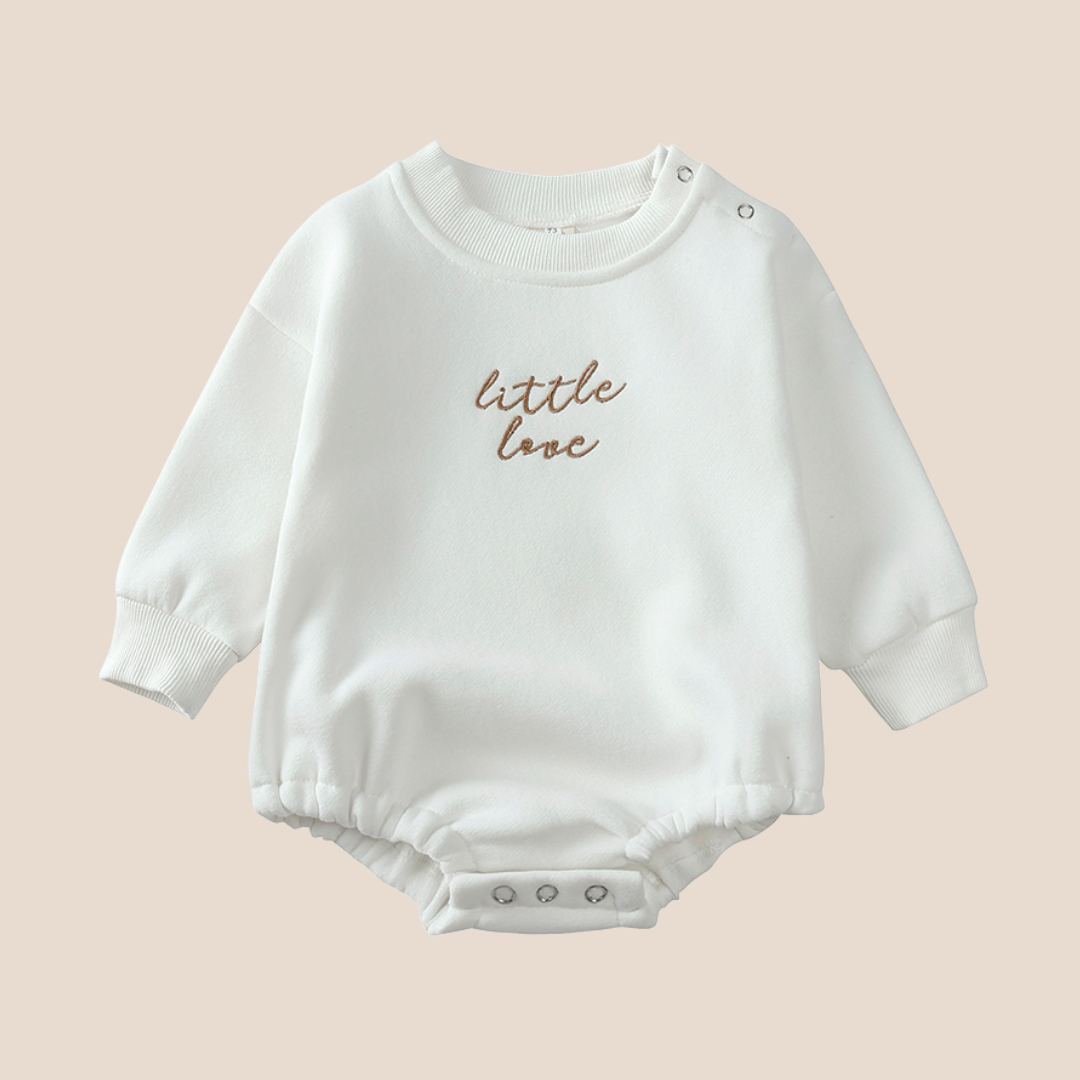 White baby romper with 'little love' text on a beige background
