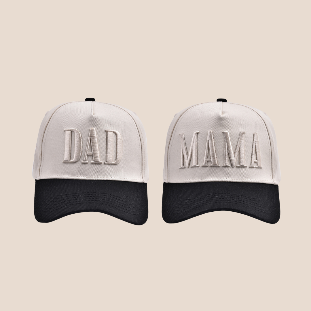 Two baseball caps, one with 'DAD' and the other with 'MAMA', on a beige background.
