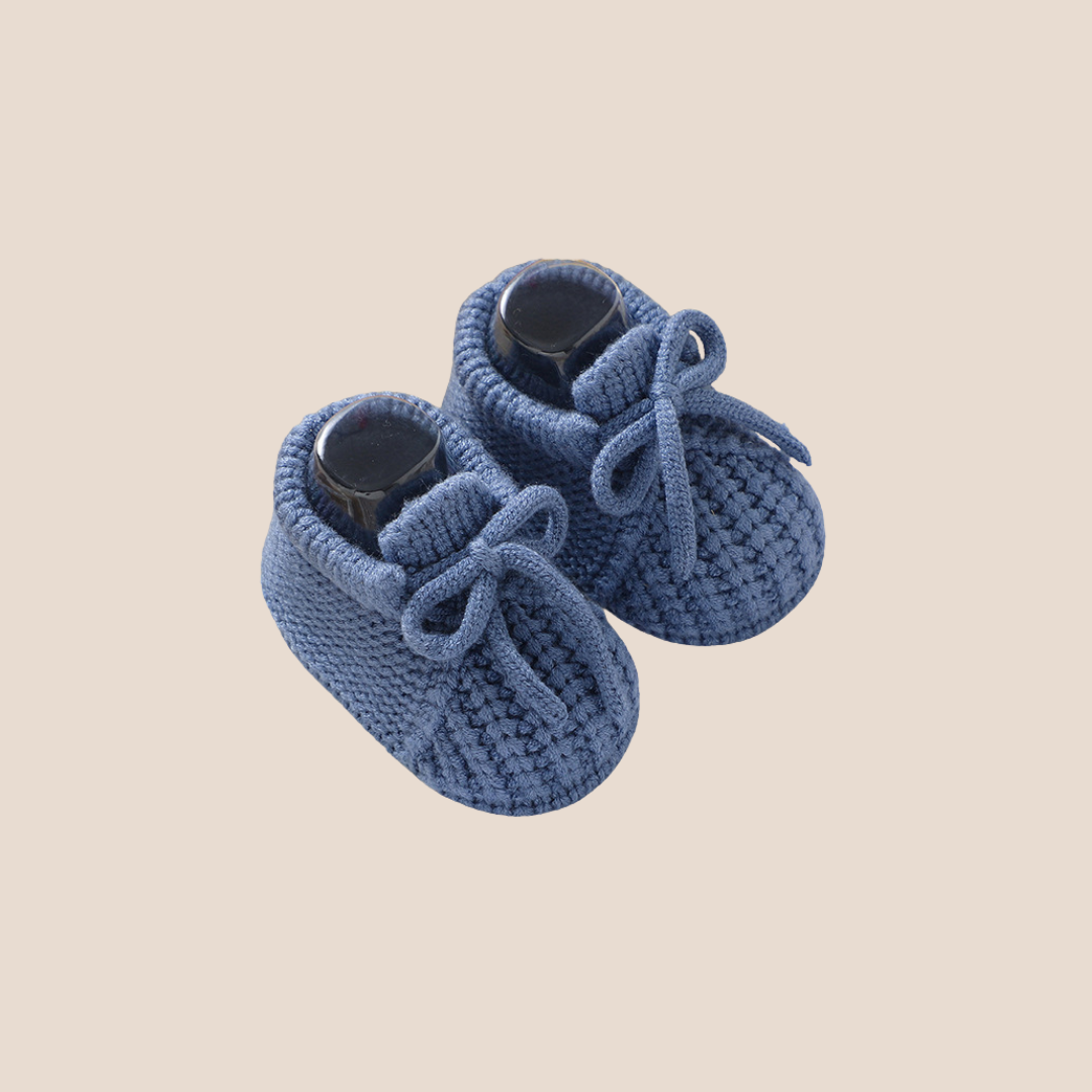 Pair of blue knitted baby shoes on a beige background