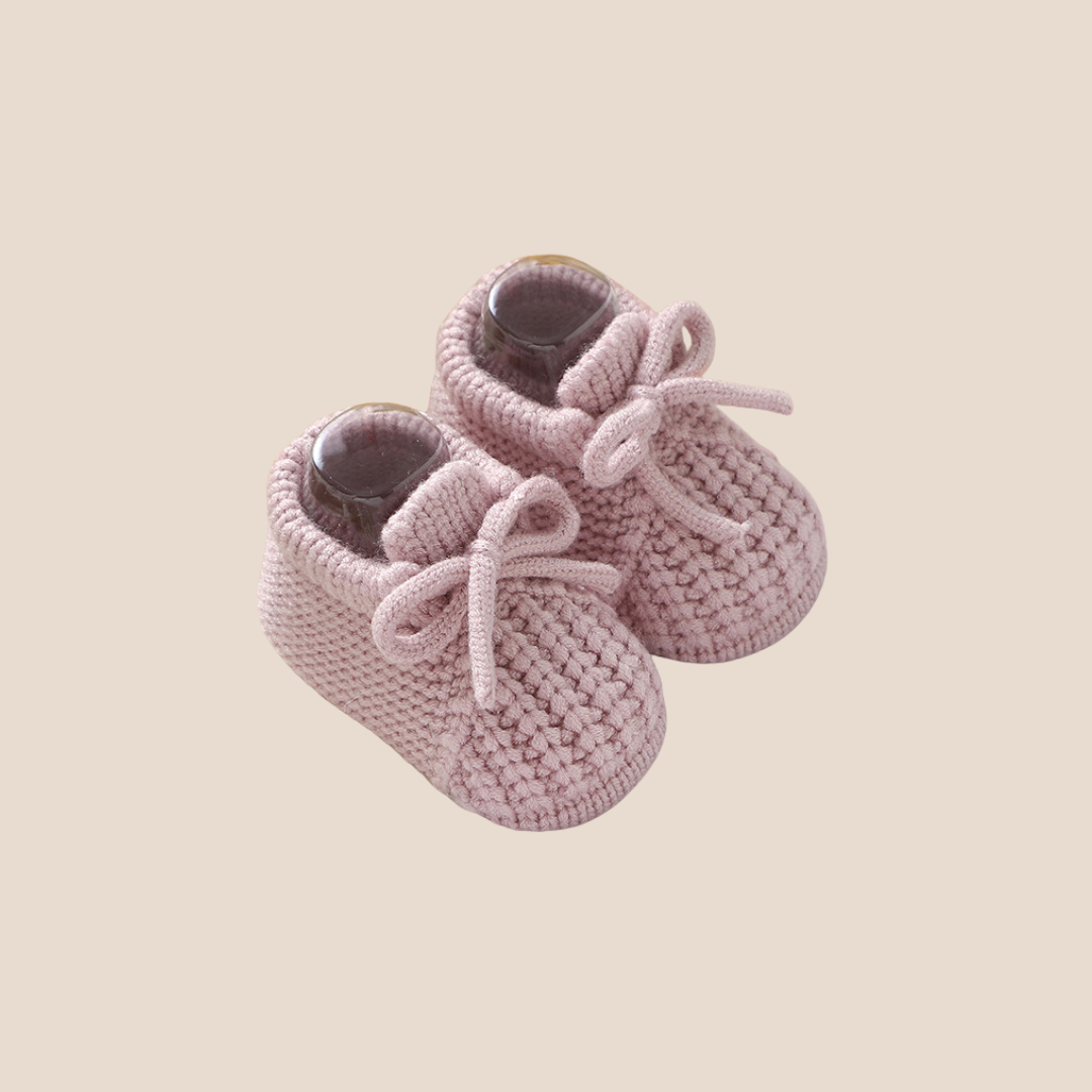 Pair of pink knitted baby shoes on a beige background