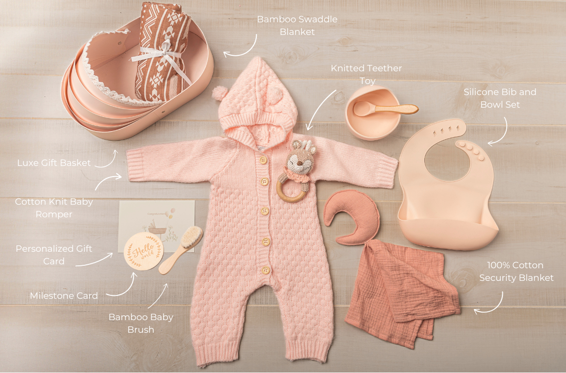Baby clothing and accessories including a pink hooded onesie, bib, and toys on a wooden surface.