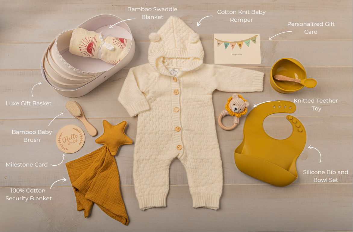 Baby clothing and accessories including a onesie, bib, and toys on a wooden surface.