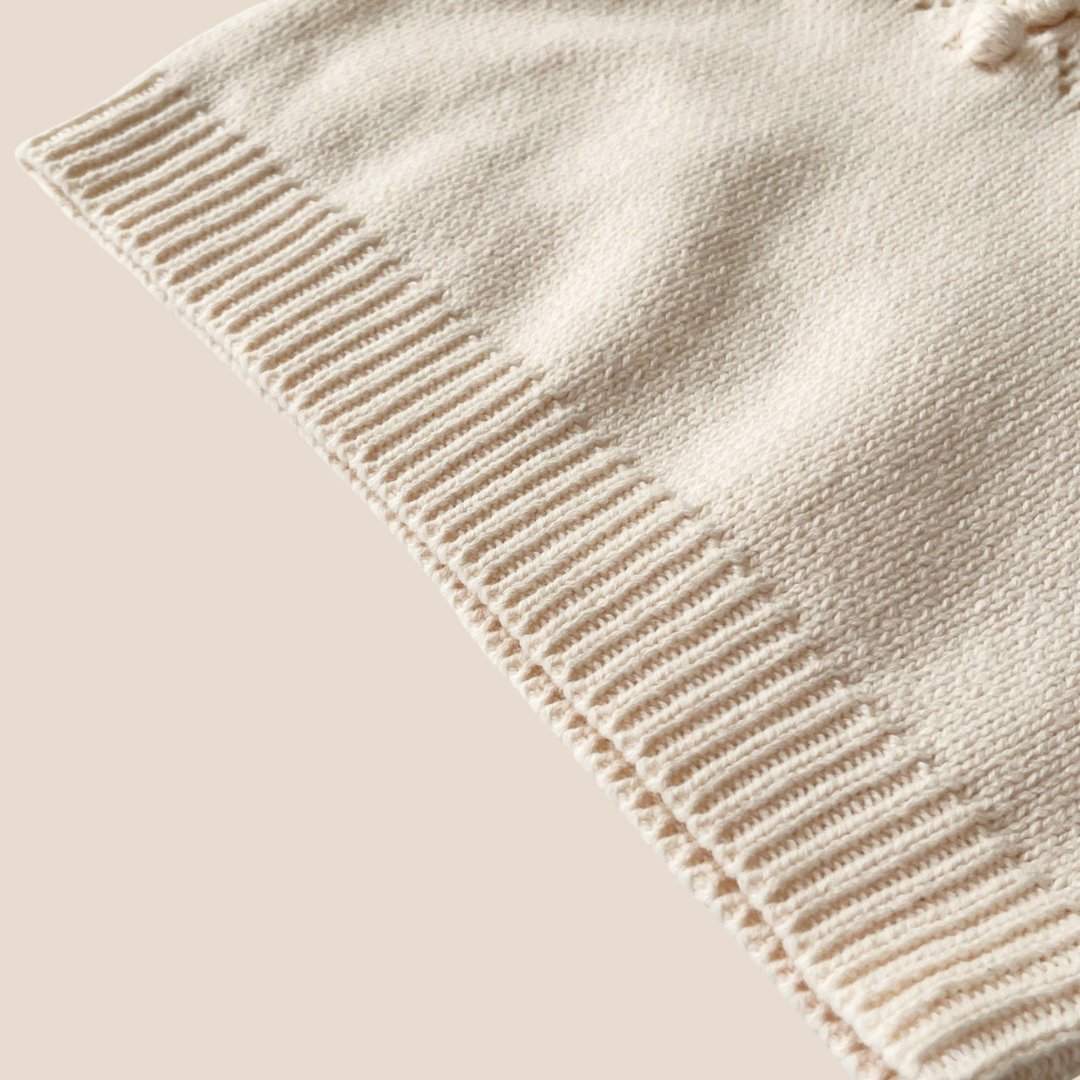 Close-up of a beige knitted sweater romper with ribbed edge on a beige background