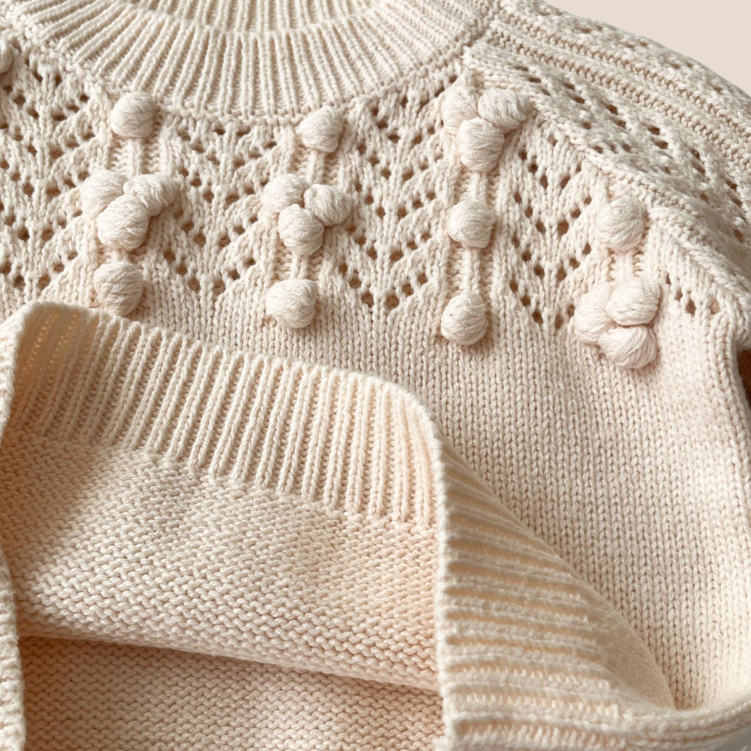 Close-up of a cream-colored knitted sweater with decorative elements.