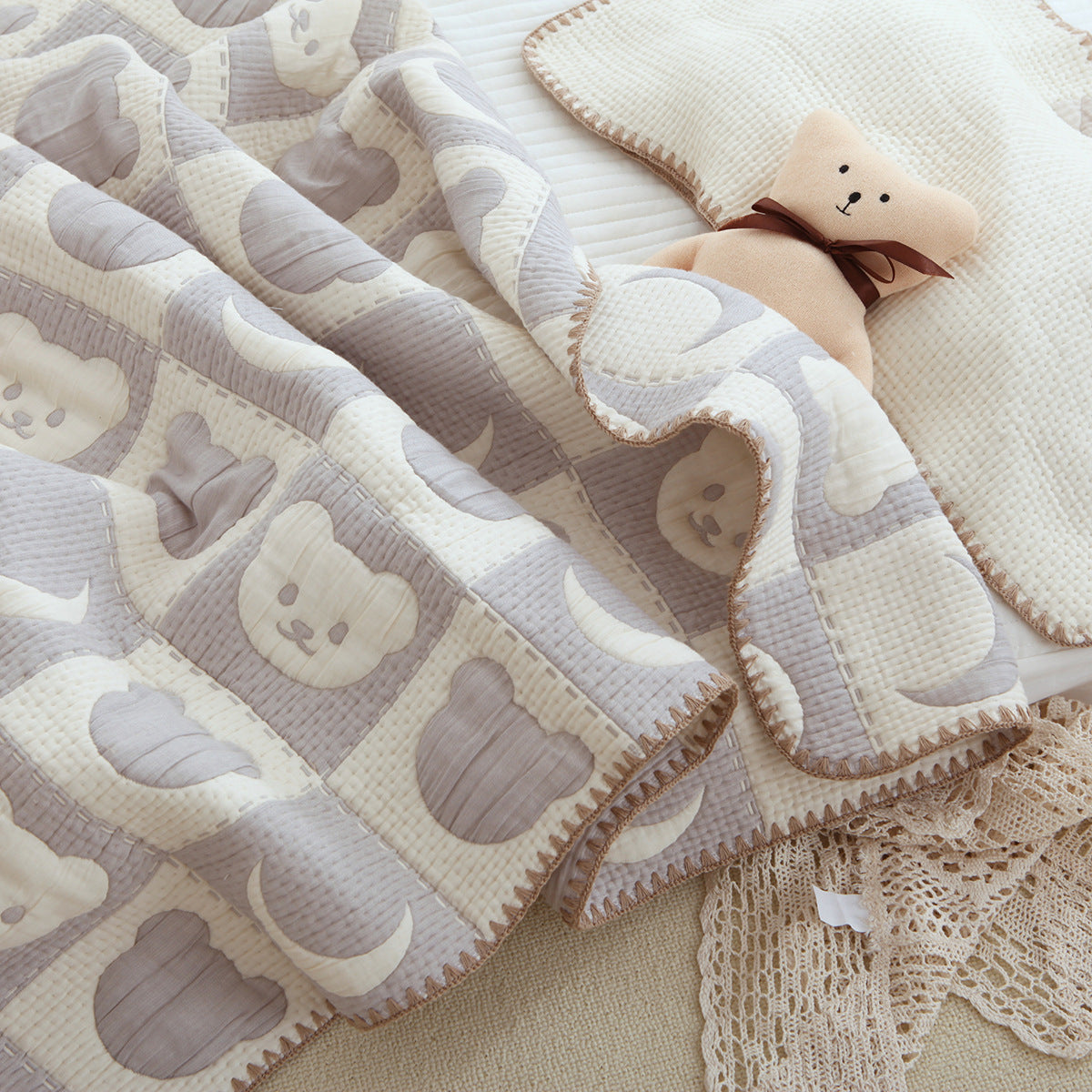 Close-up of textured quilted baby blanket with gray teddy bears, cream crescent moons, and stitched edges.
