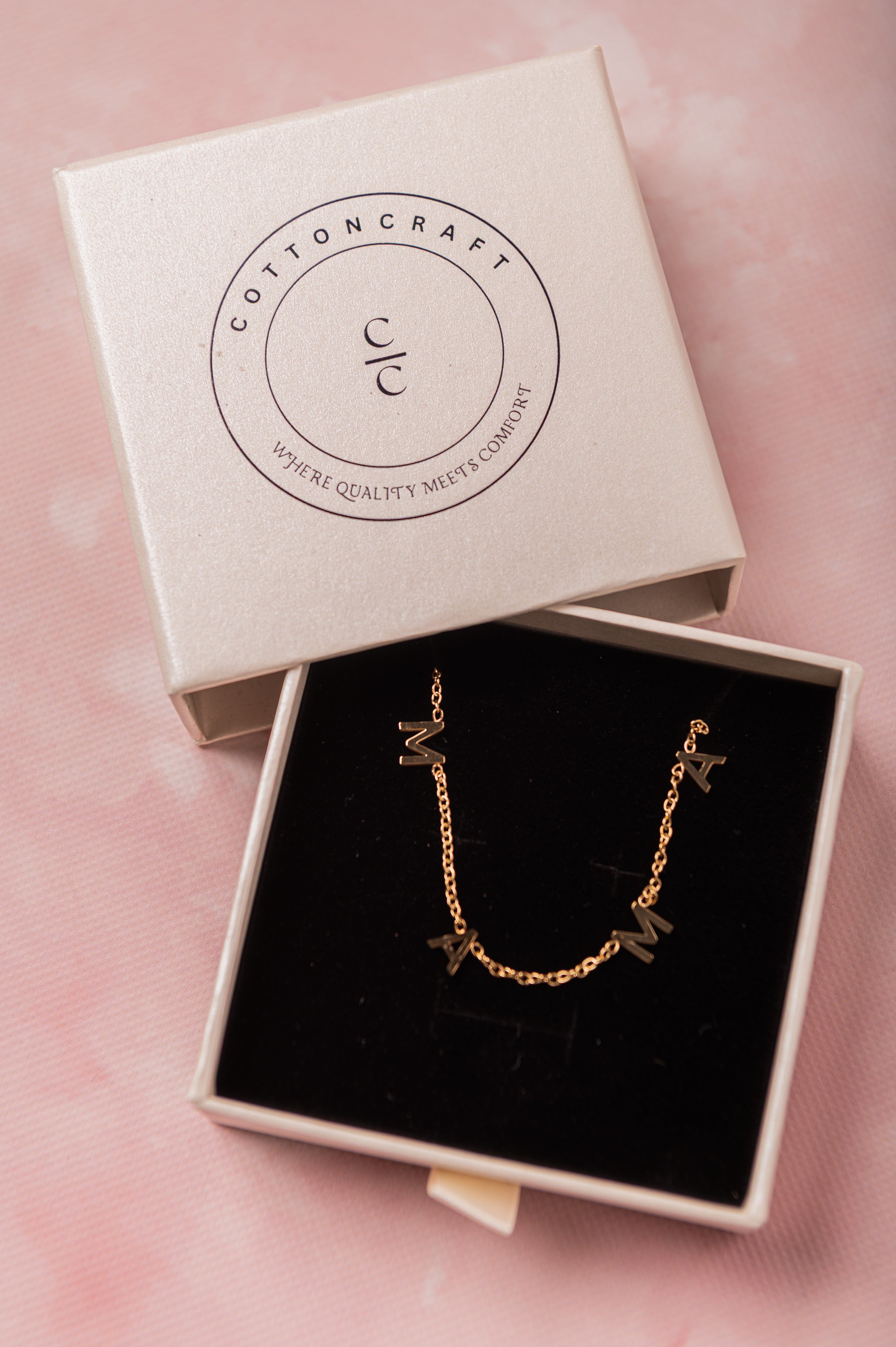 Gold necklace in an open Cotton Craft box on a pink background