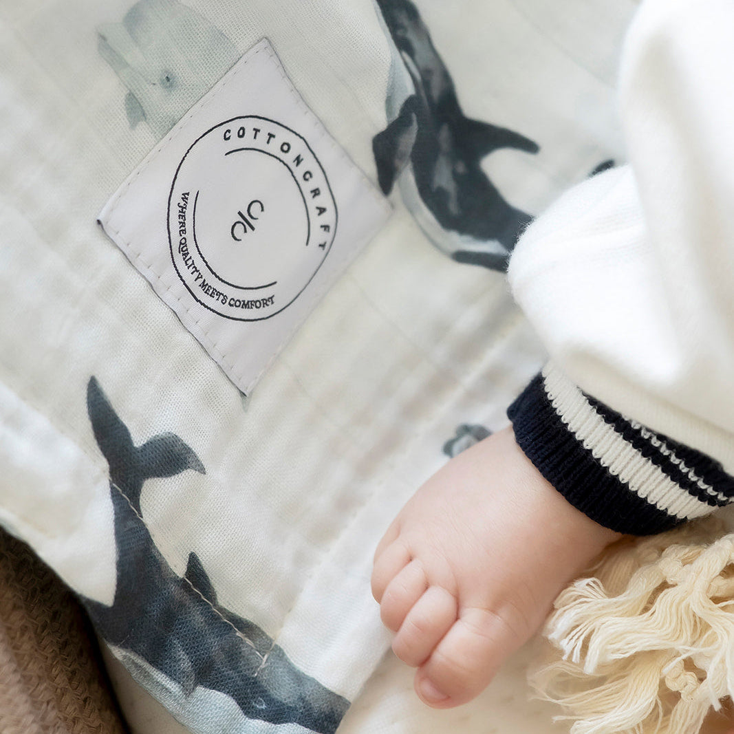 Baby's hand on a blanket with whale pattern and Cotton & Steel label