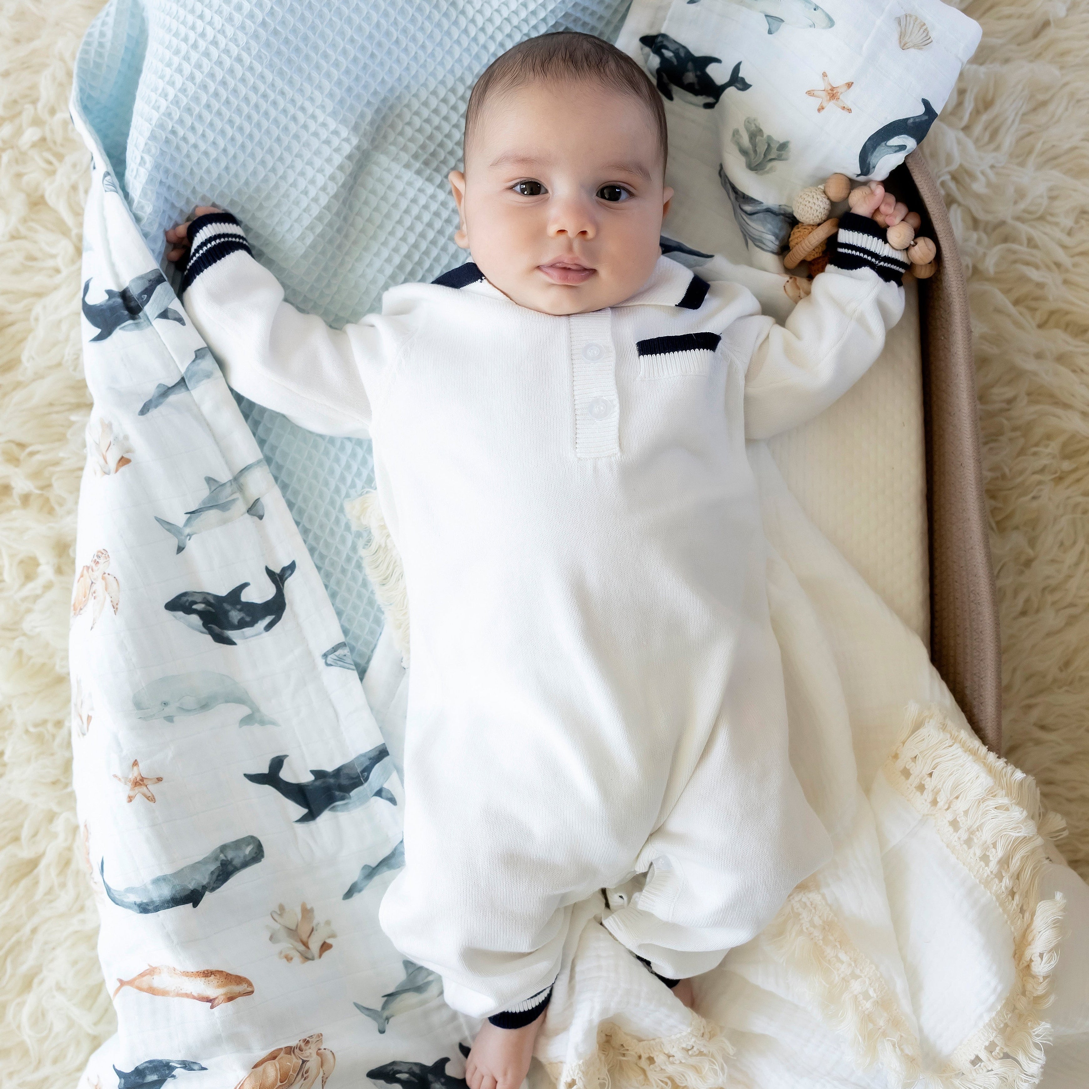 Baby in a white onesie surrounded by patterned blankets on a soft surface