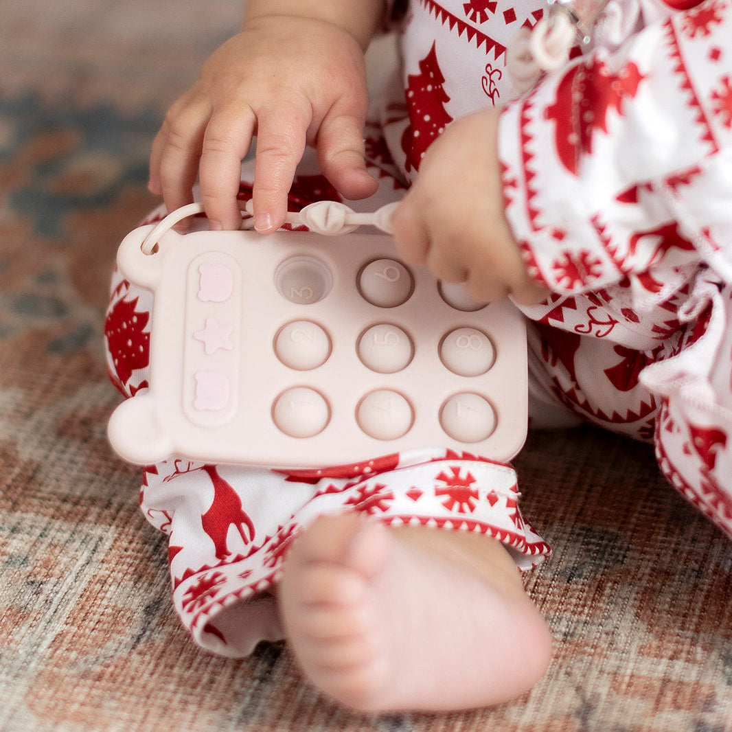 Child playing with a pink pop-it toy wearing red and white pajamas.